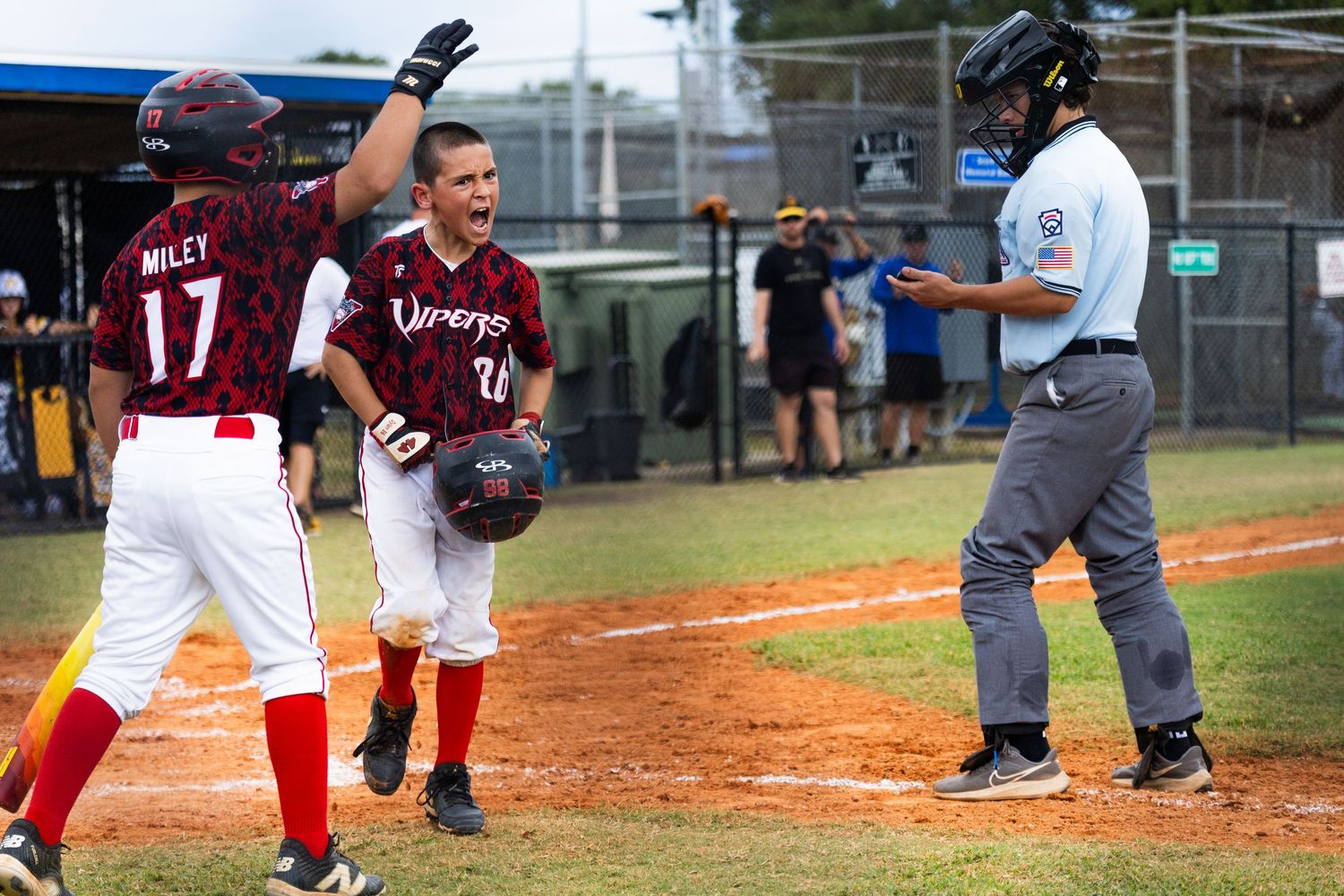 Youth baseball players and umpires gather on the baseball field during a game.
