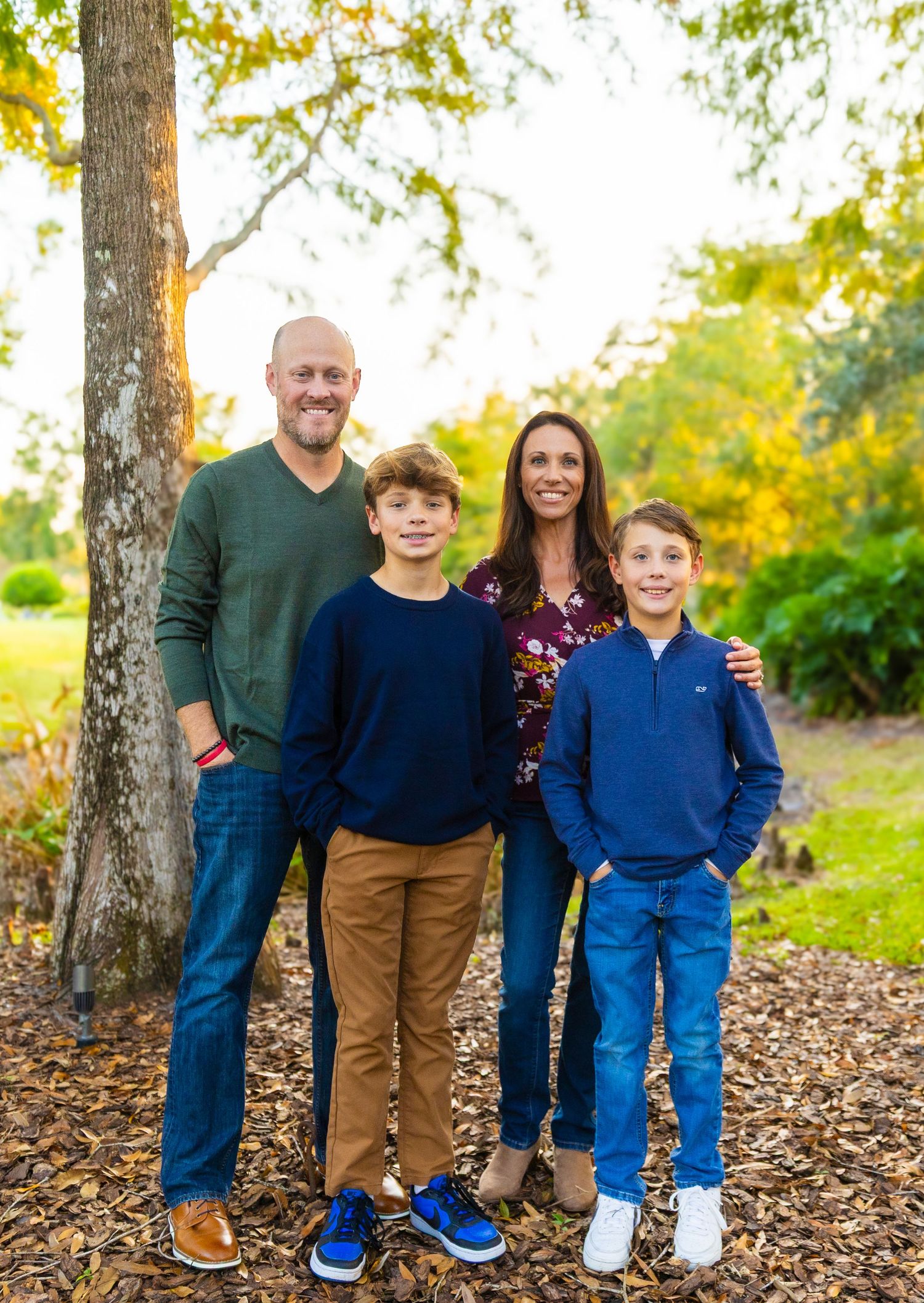 Family poses together on fallen autumn leaves in a park setting during golden hour.