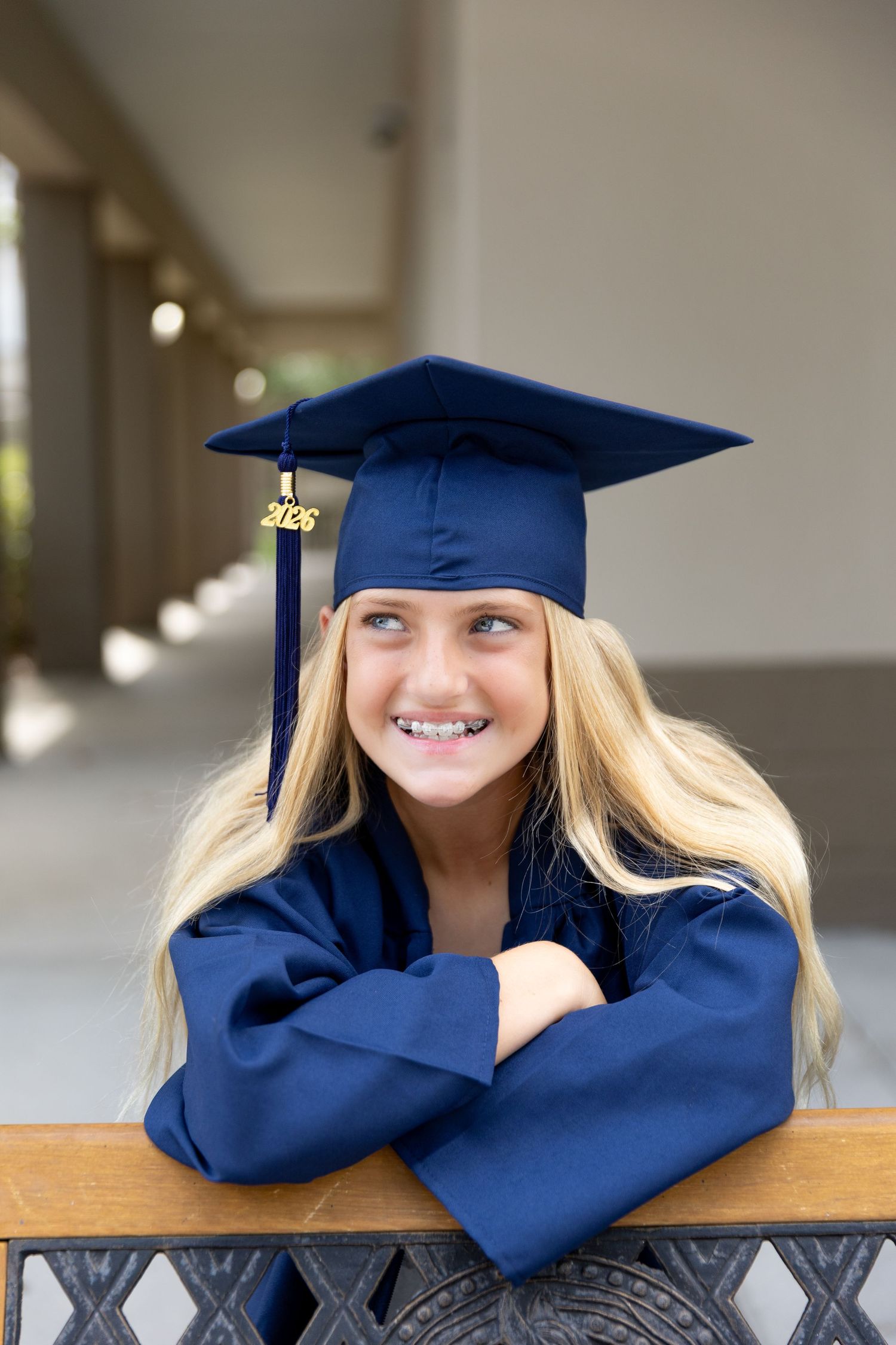 Smiling girl in navy blue graduation cap and gown with 2026 tassel, arms crossed, posing outdoors.