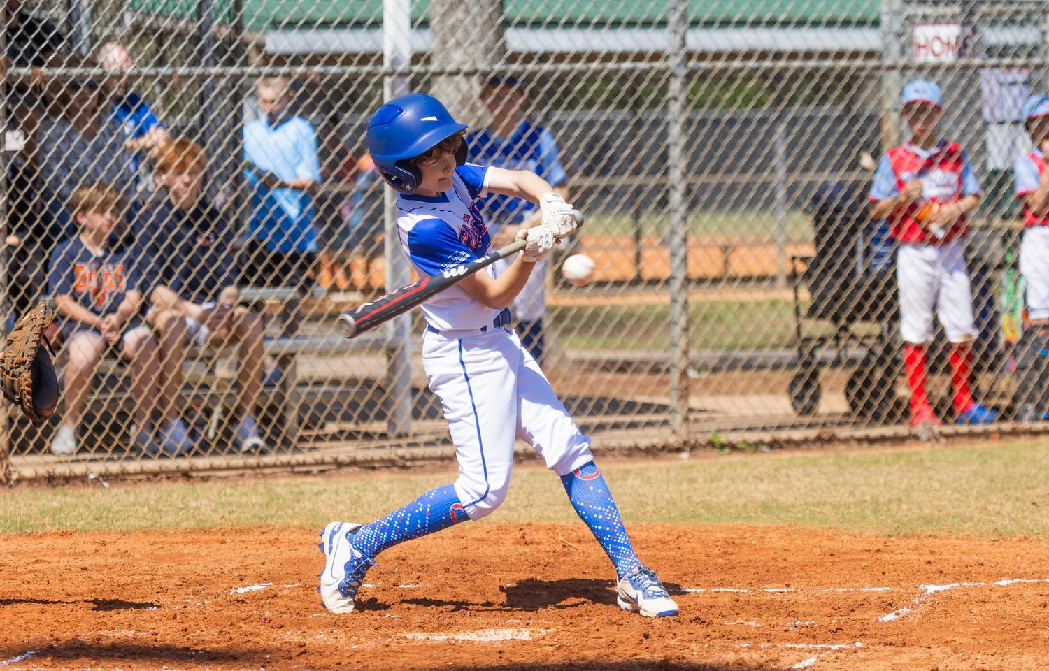 Baseball player in blue jersey swings bat during game on dirt field with spectators watching.