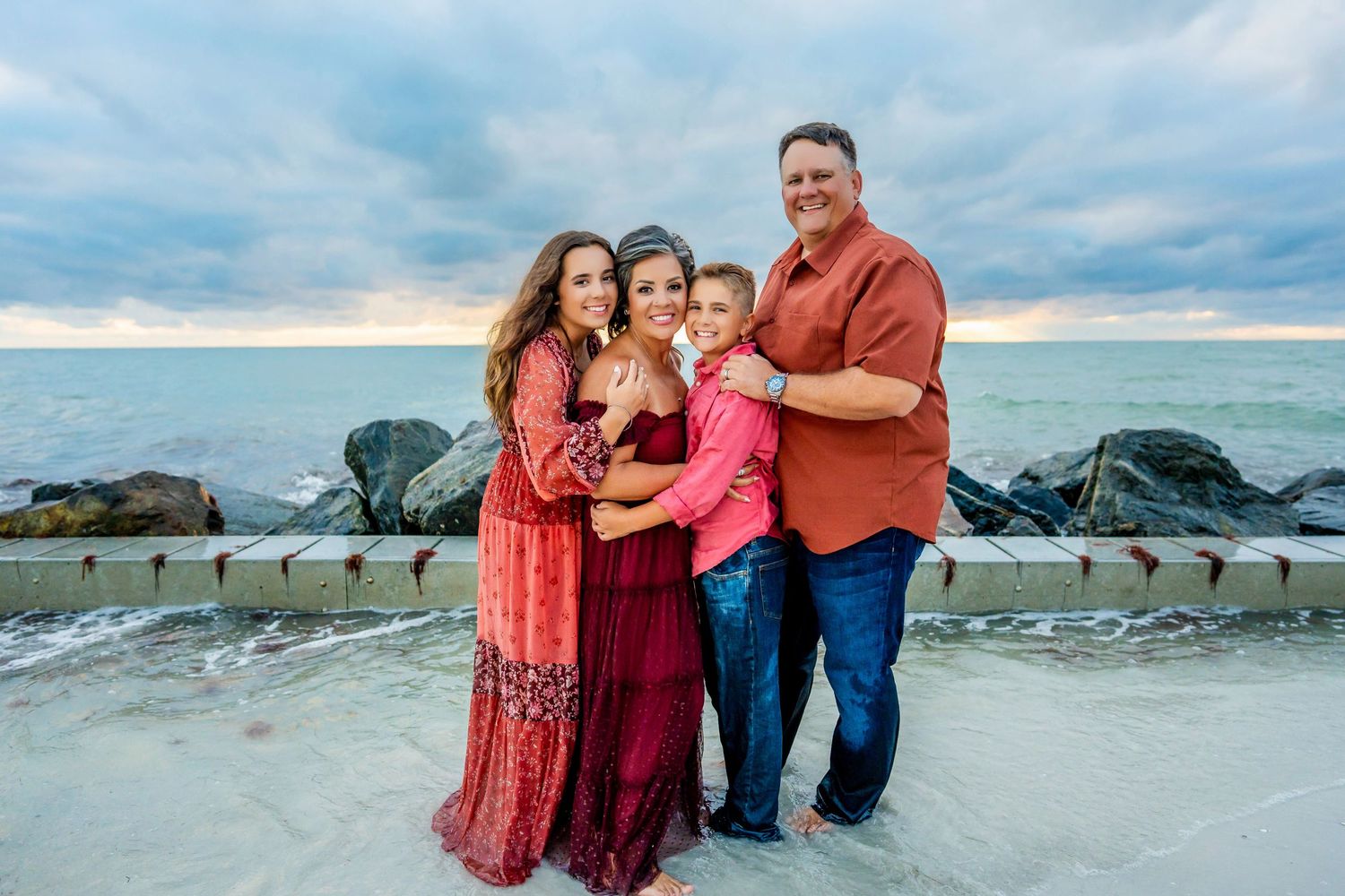 Family portrait session at sunset on beach with coordinated red and blue outfits.