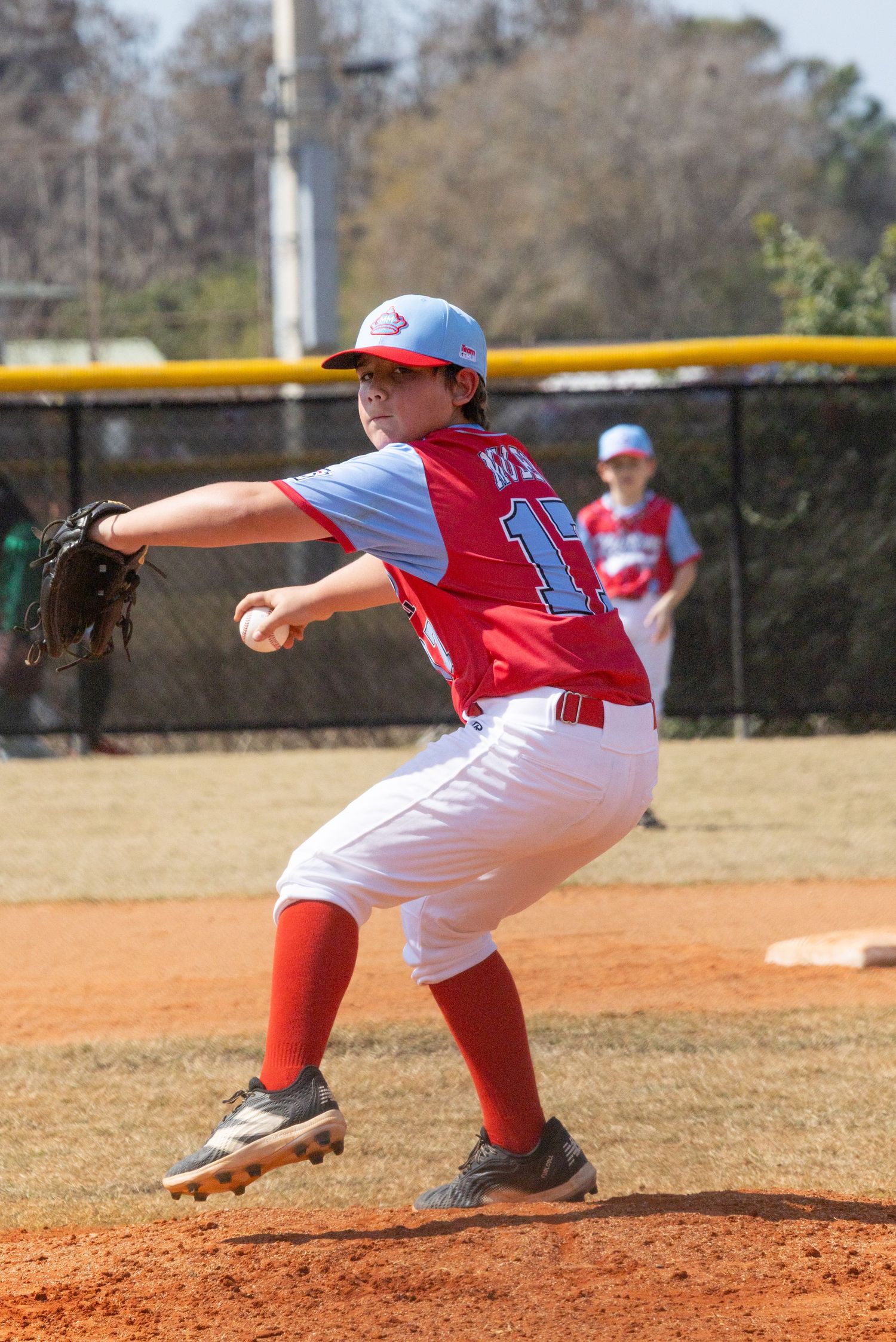 Baseball pitcher in red and white uniform demonstrating throwing motion sequence.