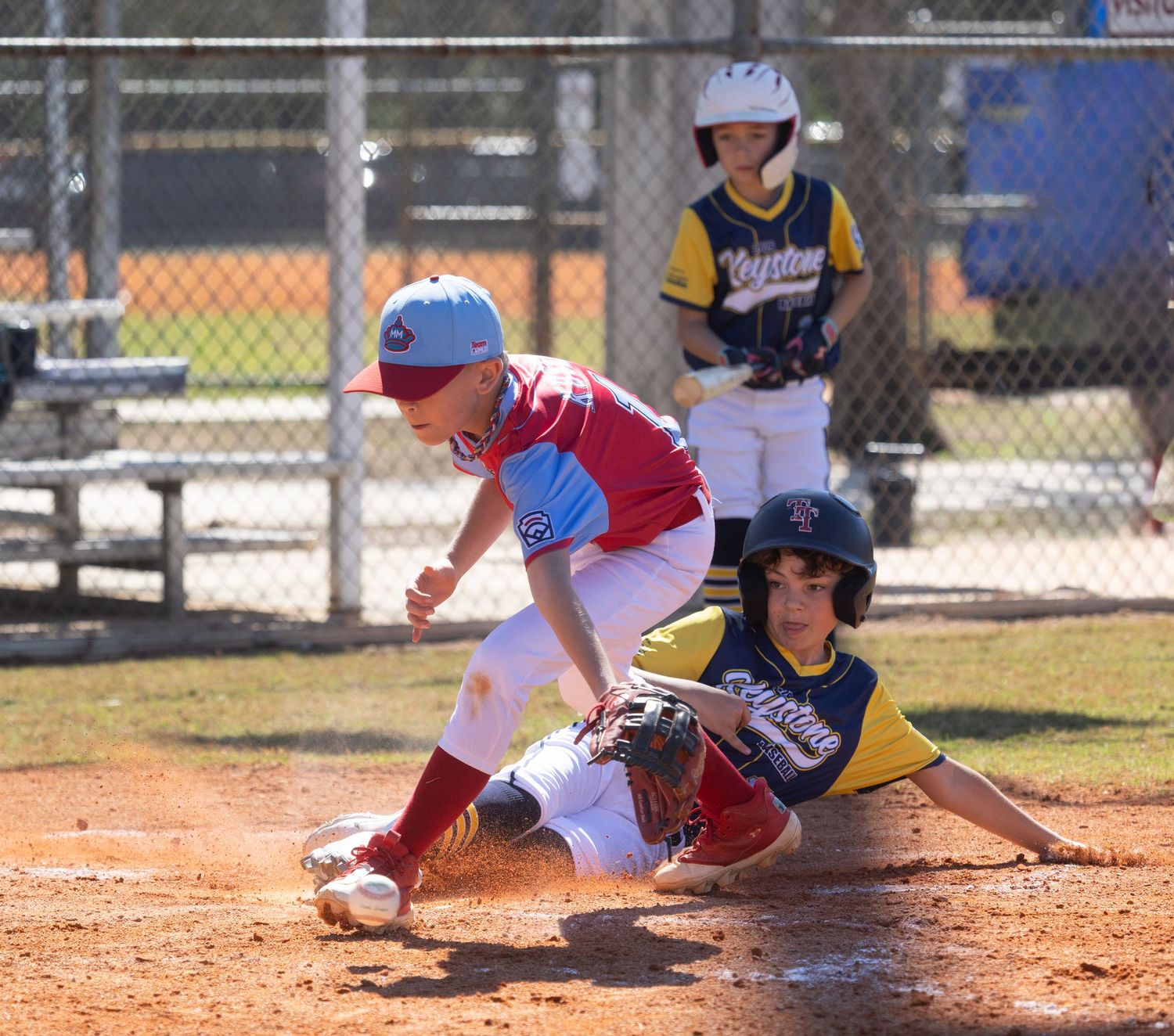 Baseball players collide in dramatic play at home plate during youth game.