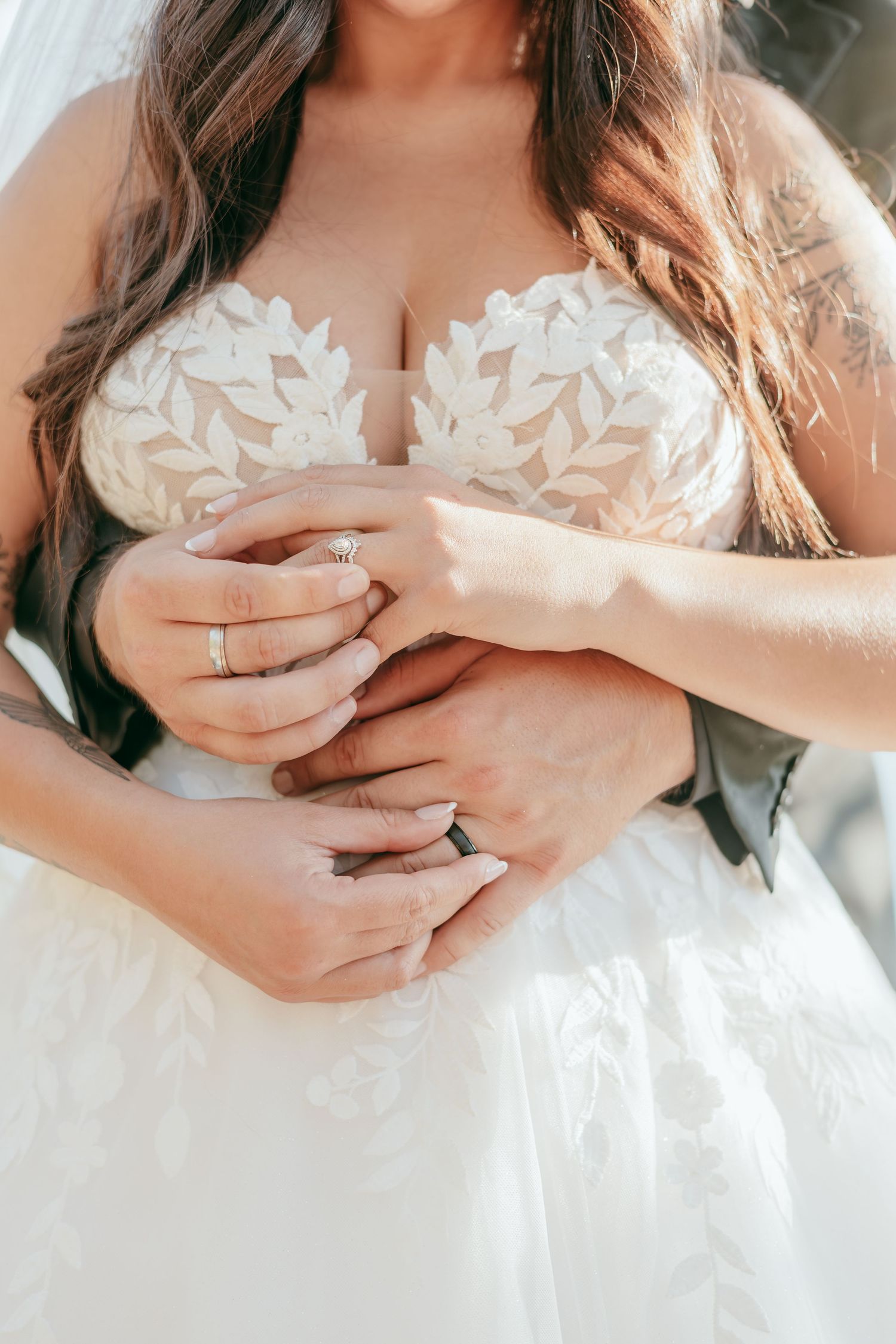 Close-up of bride and groom holding hands showing wedding rings, bride in lace bodice gown.