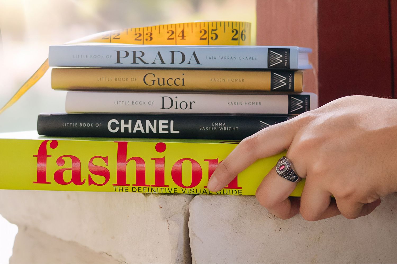 Stack of luxury fashion books including Chanel, Dior, Gucci, and Prada with hand reaching in.