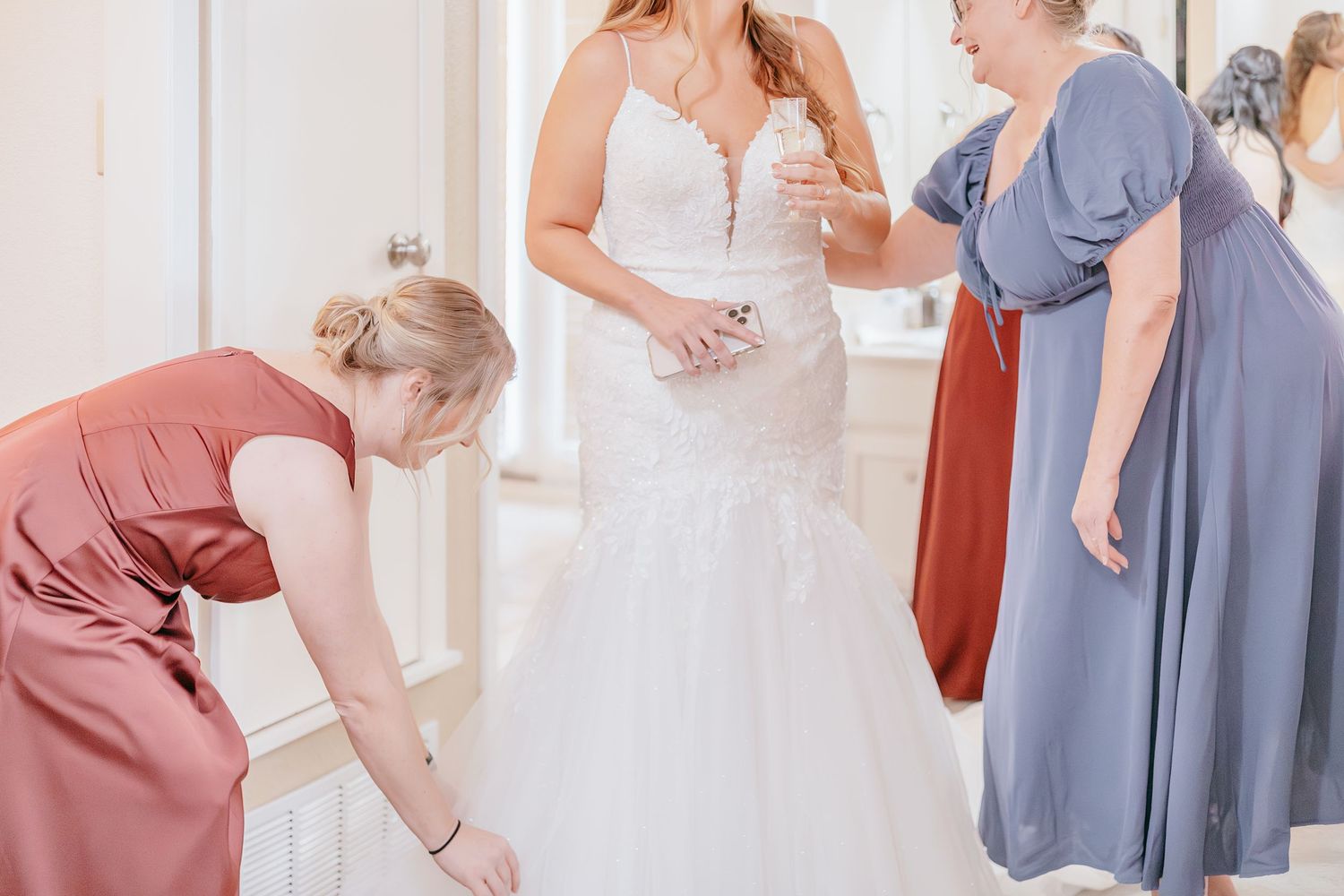 Bridesmaids helping the bride get ready in her white lace wedding dress on the wedding day.
