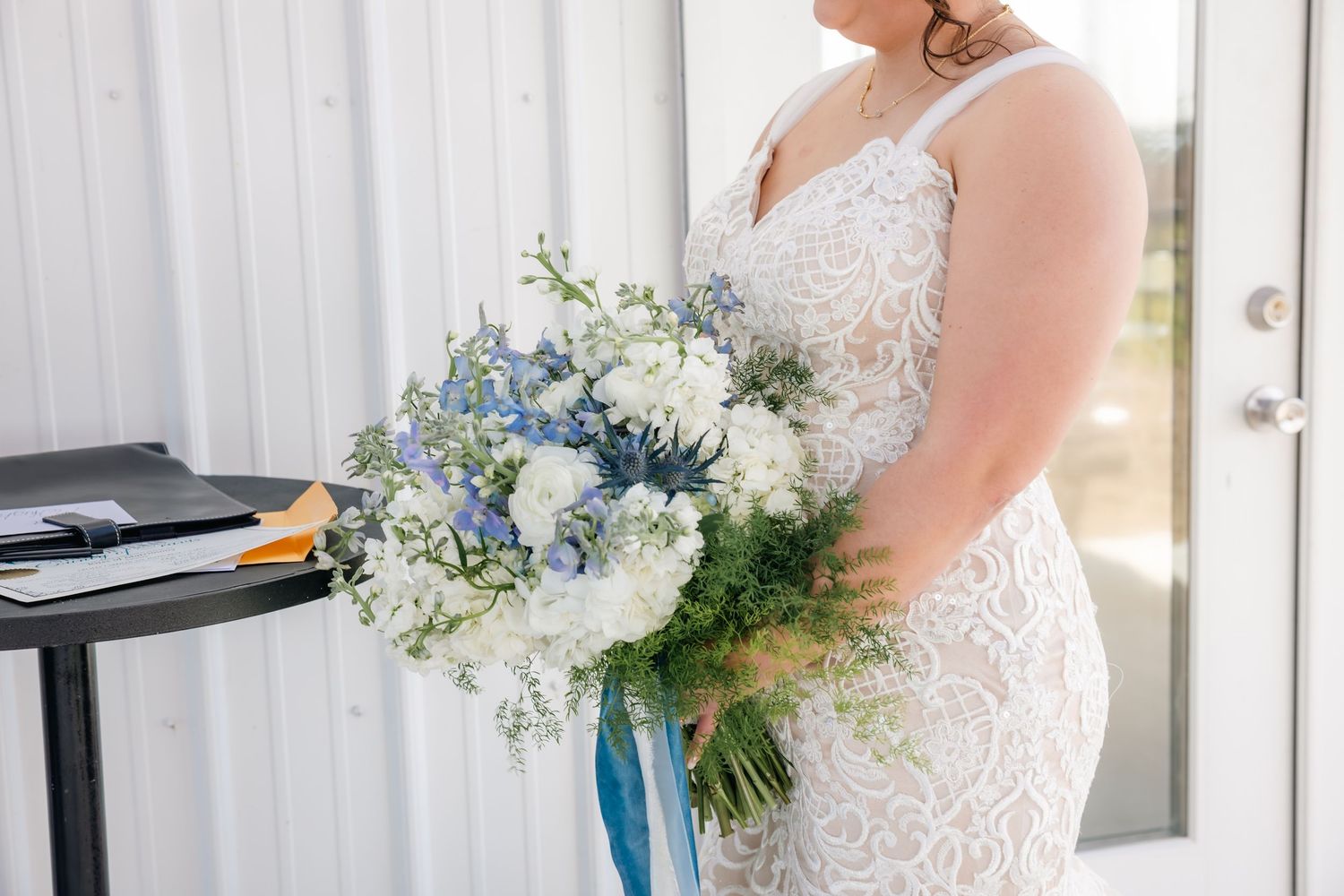 Bride in lace mermaid gown holds a stunning bouquet of white and blue wedding flowers.