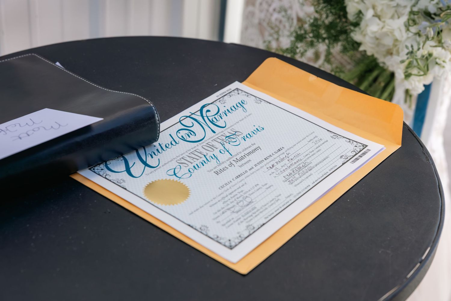Elegant wedding certificate in teal calligraphy on gold envelope displayed on dark round table.