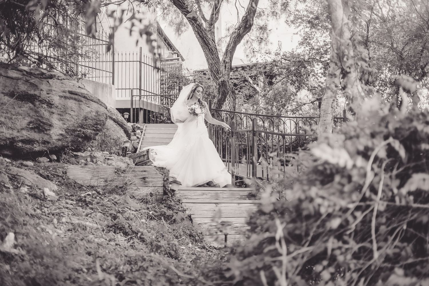 Black and white photo of bride in flowing gown walking down outdoor stone steps.