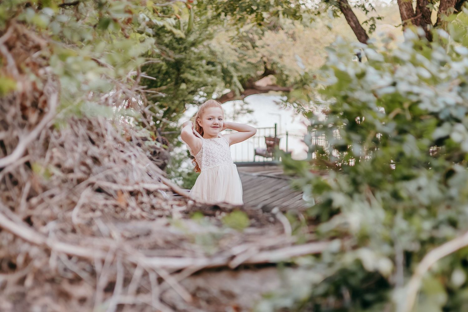 Adorable little girl in a white dress playing among lush green foliage at a wedding venue.
