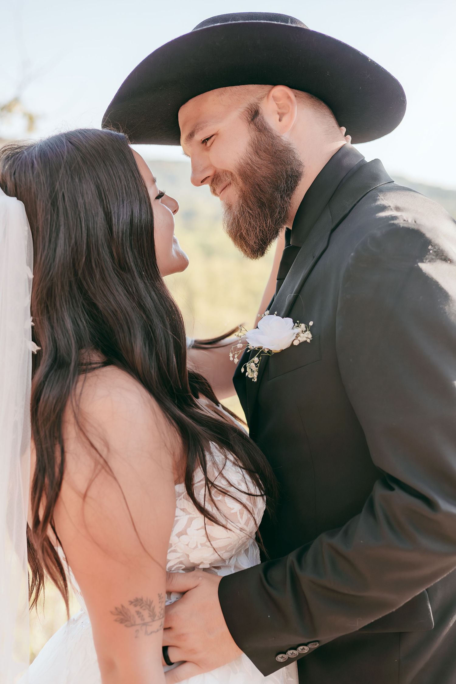 Smiling bride and bearded groom in black cowboy hat gazing lovingly at each other on wedding day.