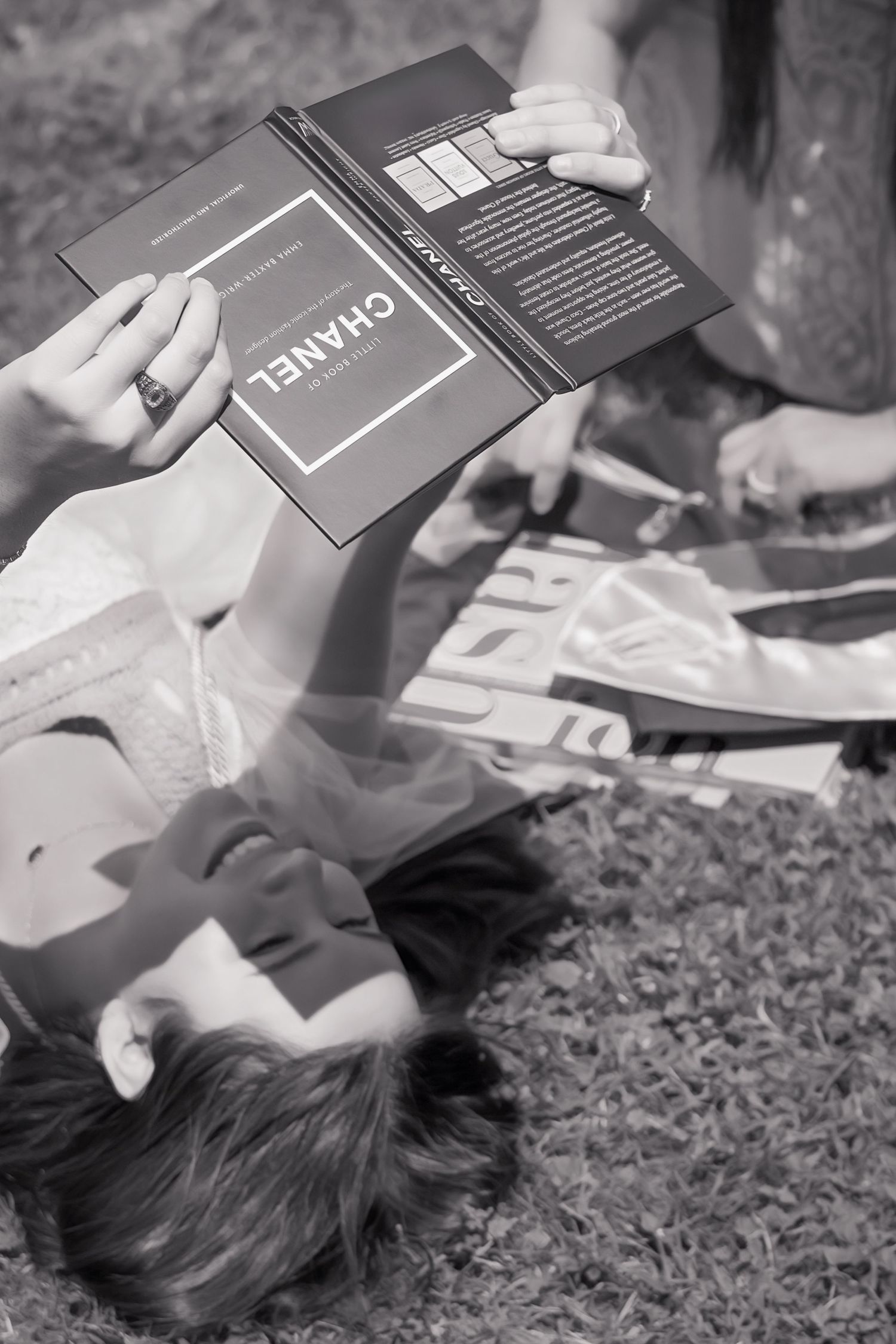 Woman lying on grass reading a Chanel fashion book, black and white photography.