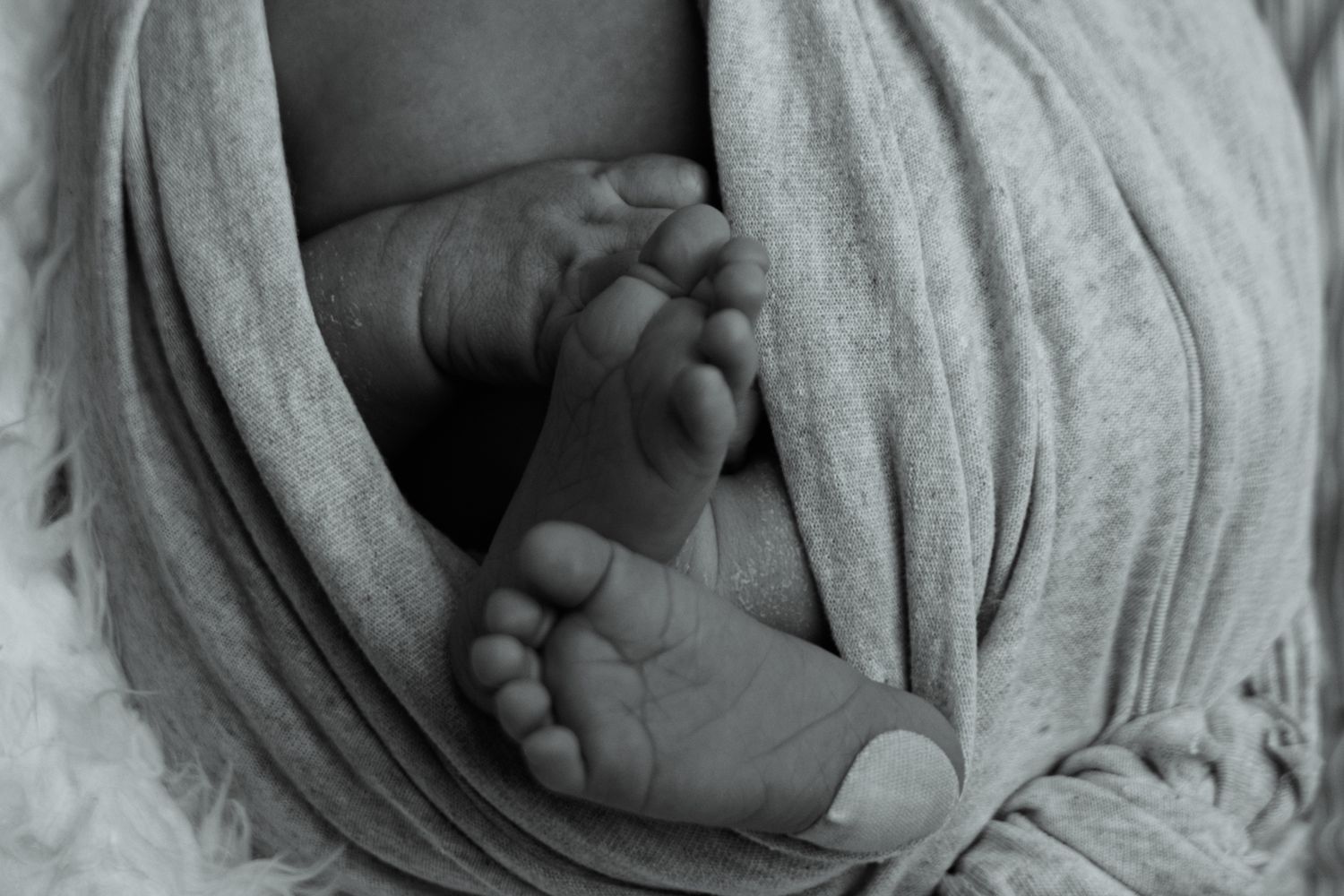 Black and white newborn baby feet wrapped in soft swaddle blanket, close-up photography.