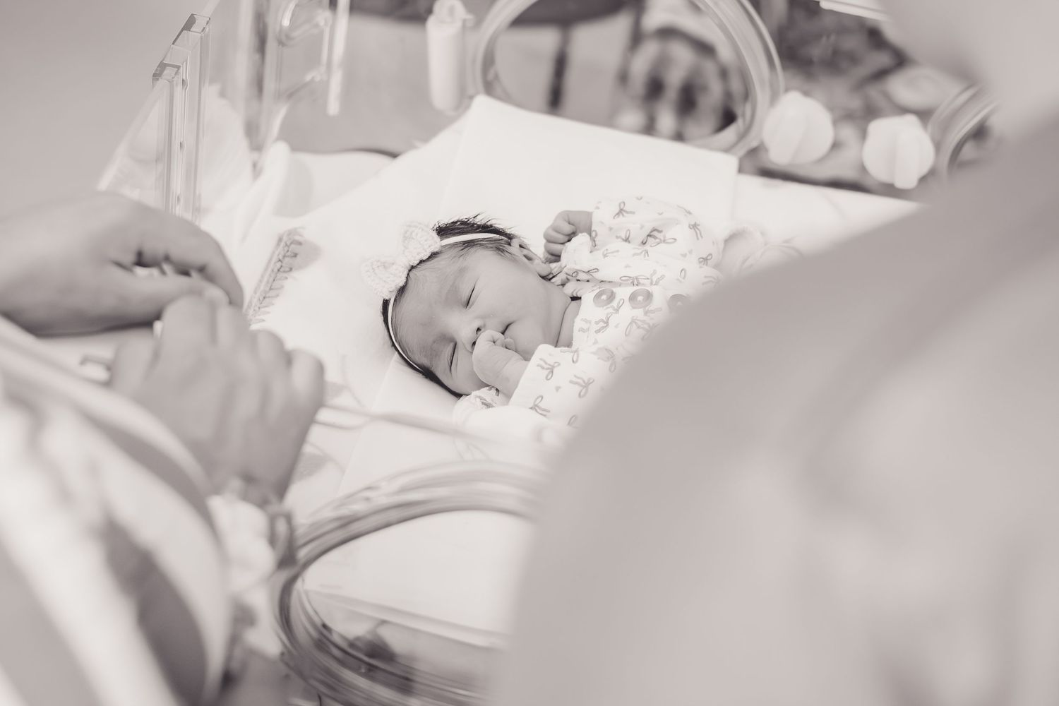 Black and white photo of a peaceful newborn baby sleeping in a hospital bassinet with parents nearby.