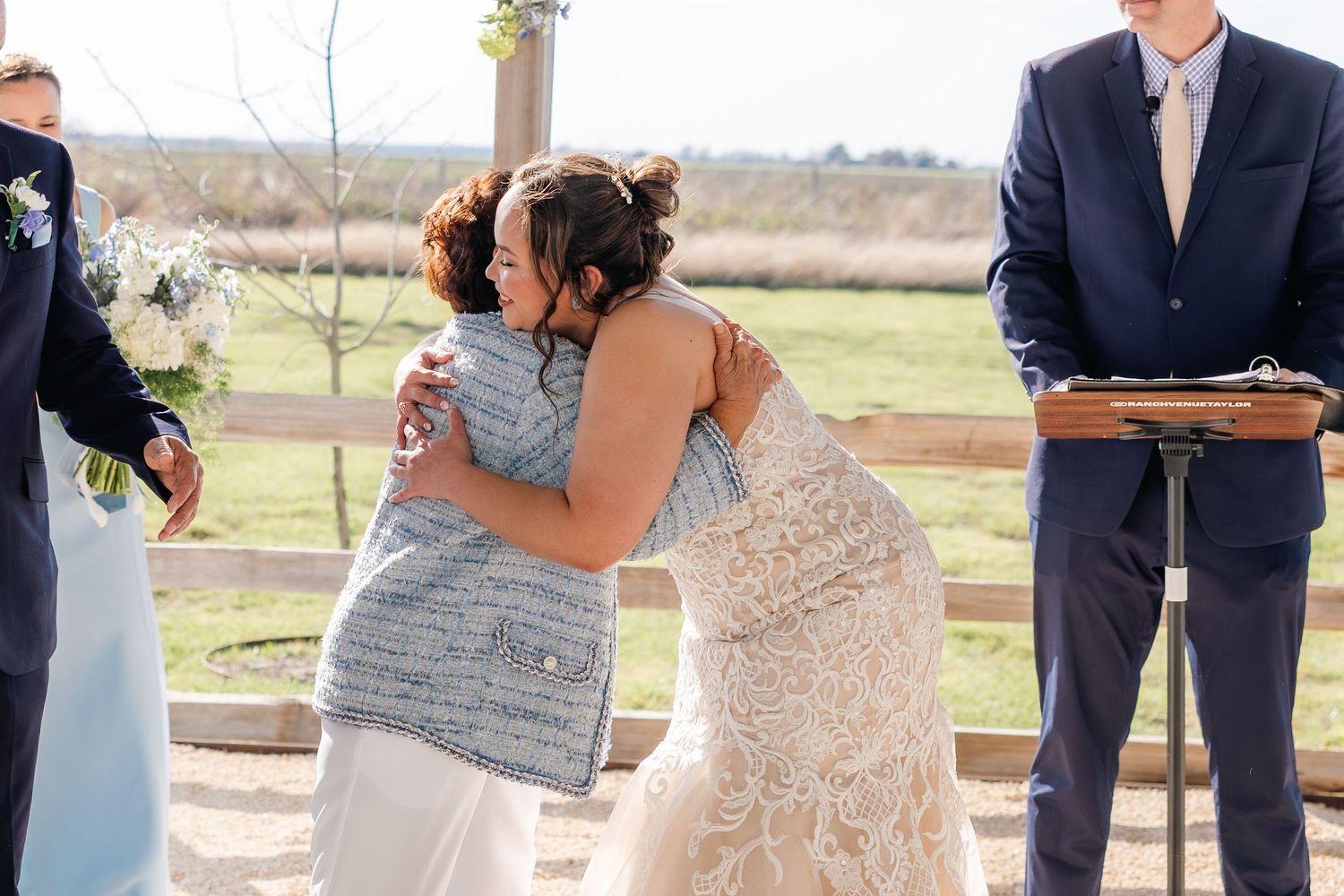 Bride shares an emotional hug with a guest during her outdoor rustic wedding ceremony.