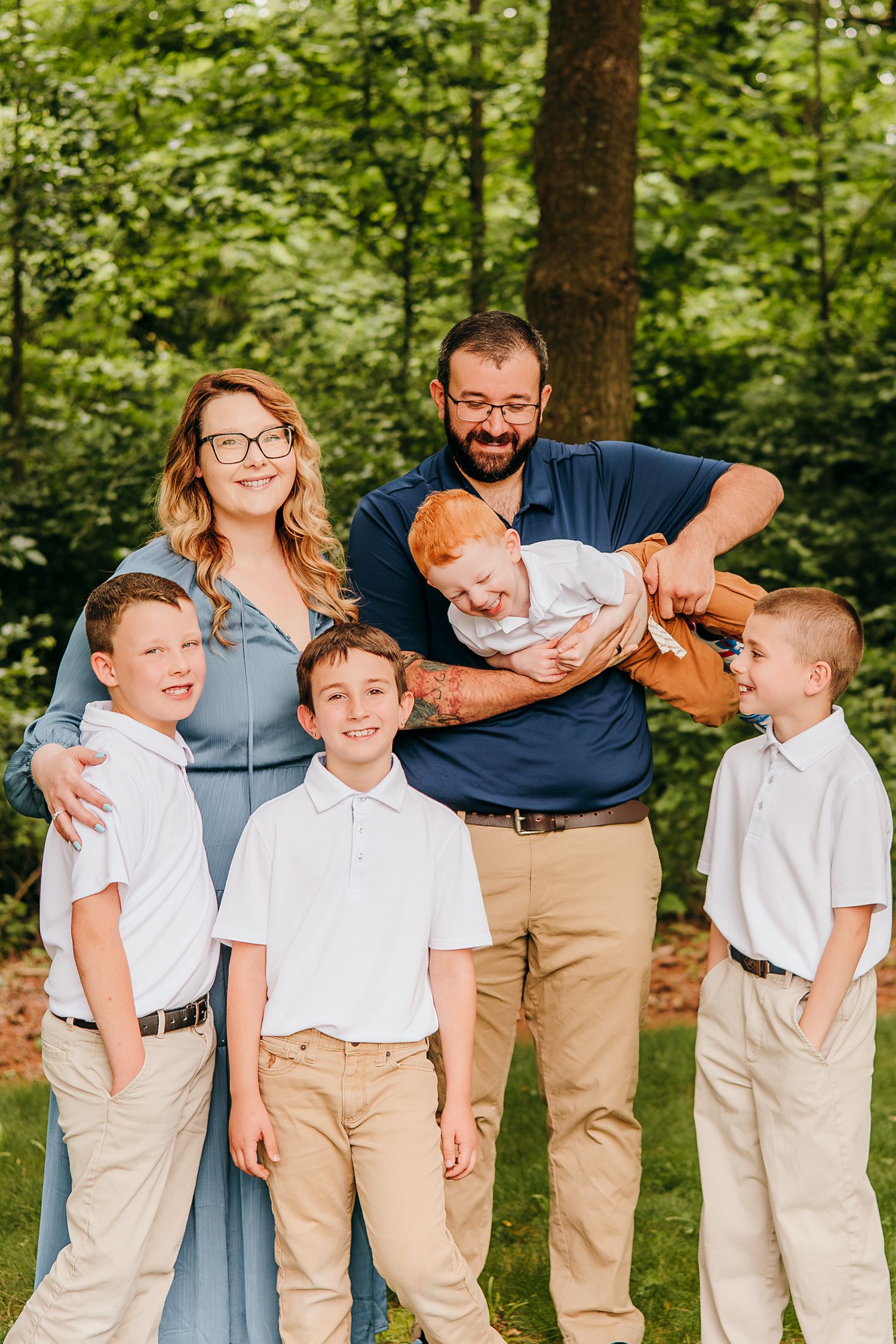 A happy family of six with four boys poses outdoors in coordinating blue and khaki outfits.