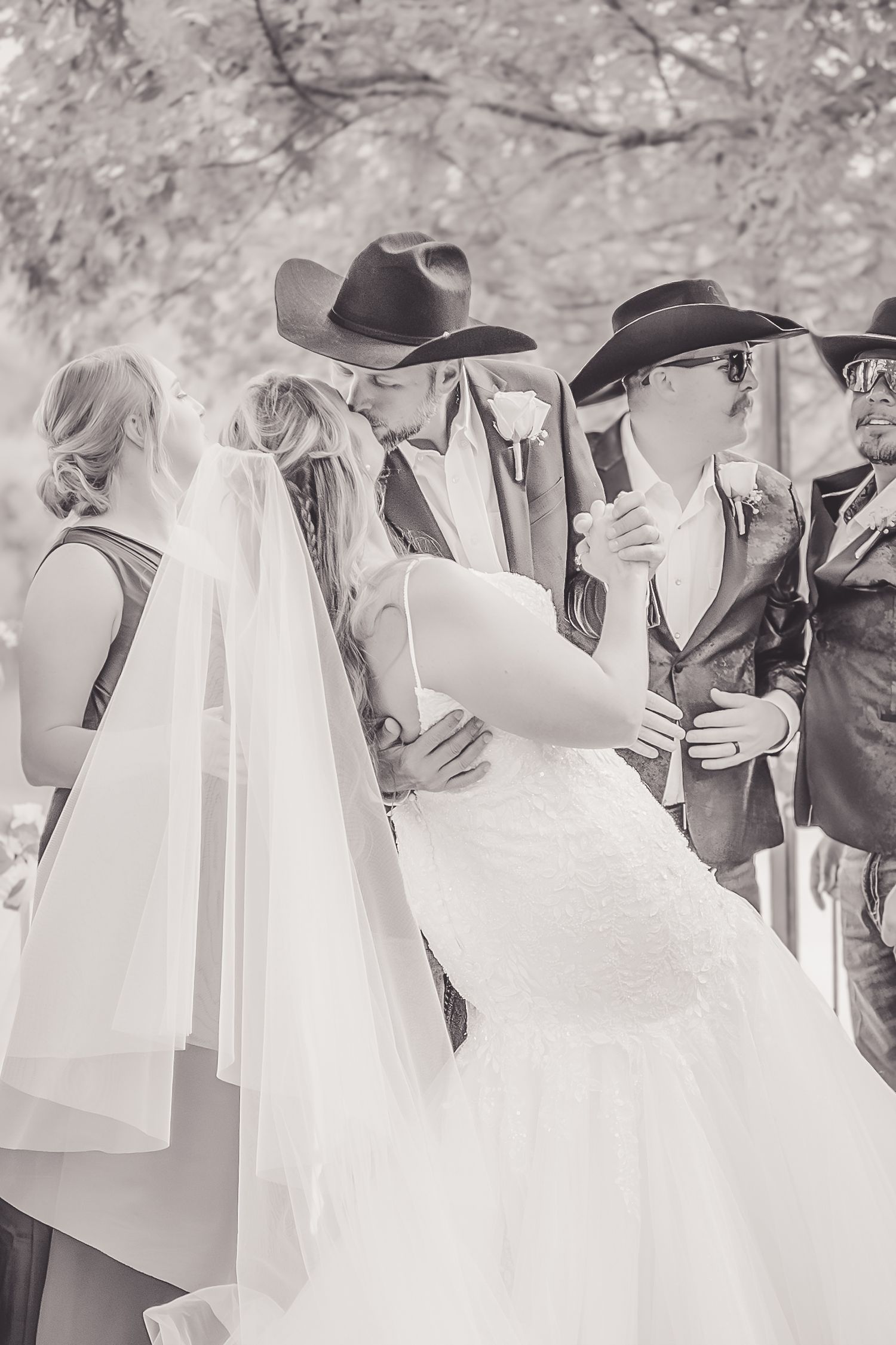 Black and white photo of bride and groom sharing first kiss at outdoor wedding ceremony.