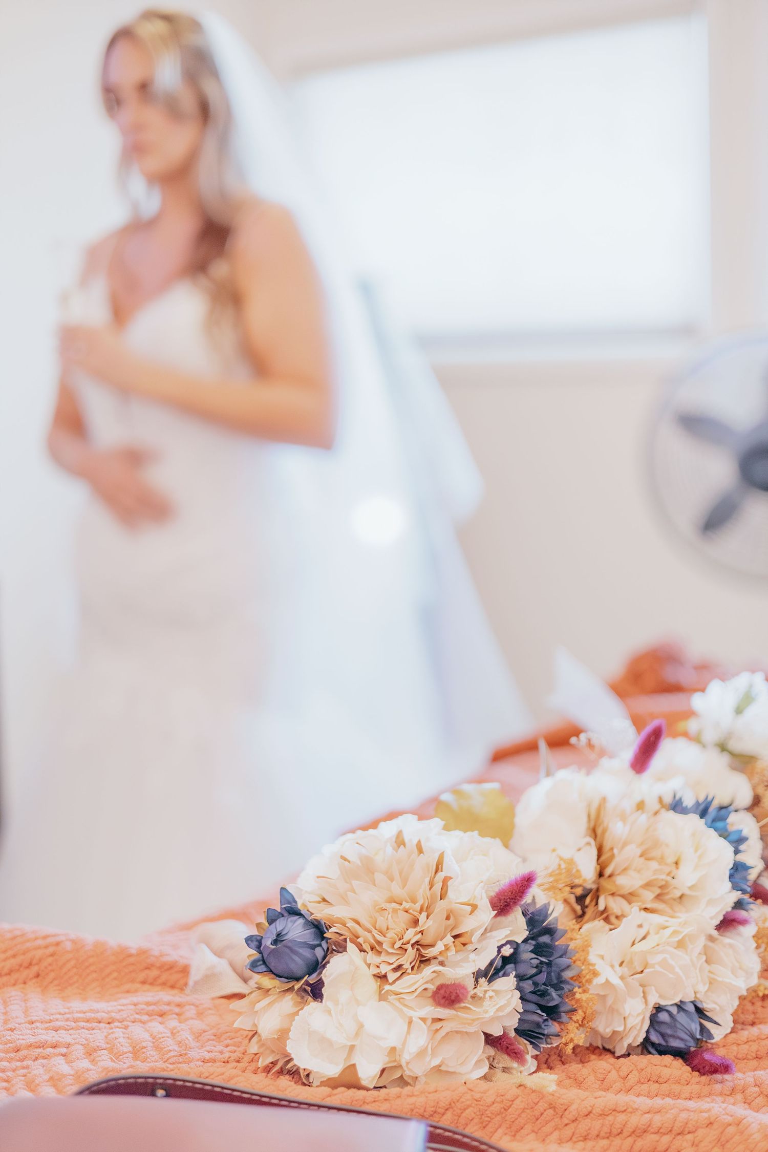 Colorful bridal bouquet with cream dahlias and blue flowers in foreground with bride in background.