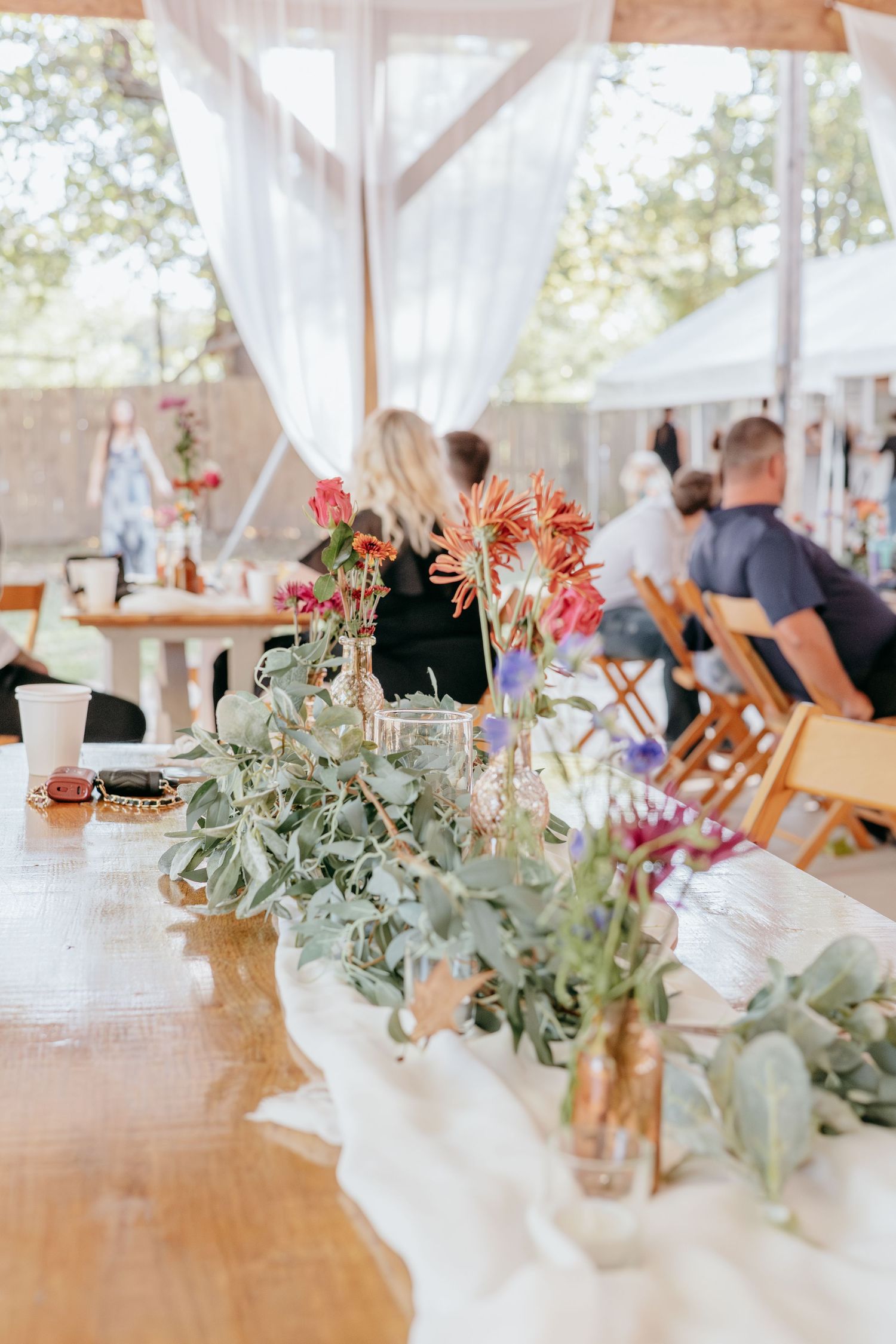 Elegant wooden reception table decorated with eucalyptus greenery and colorful flowers in gold vases at a wedding.