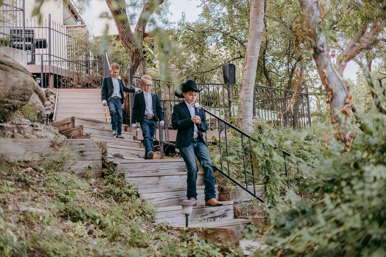 Groomsmen in suits and cowboy hats walking down wooden steps at an outdoor wedding venue.