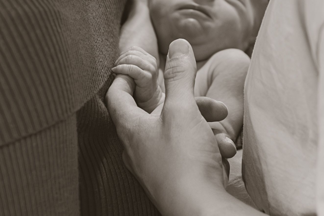 Black and white photo of a newborn baby grasping an adults finger tenderly.
