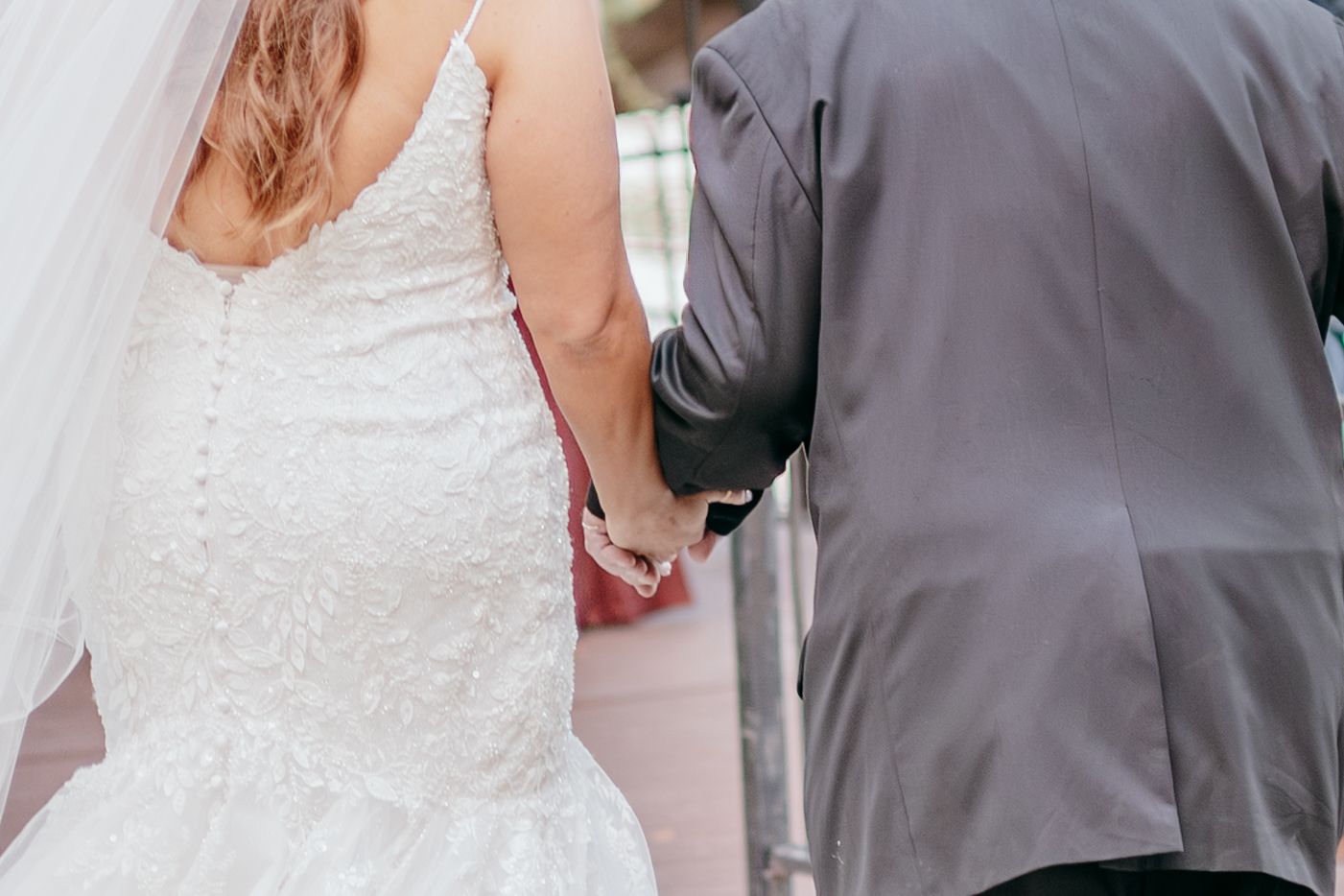 Bride in lace wedding dress holding hands with a groomsman in a gray suit at the ceremony.