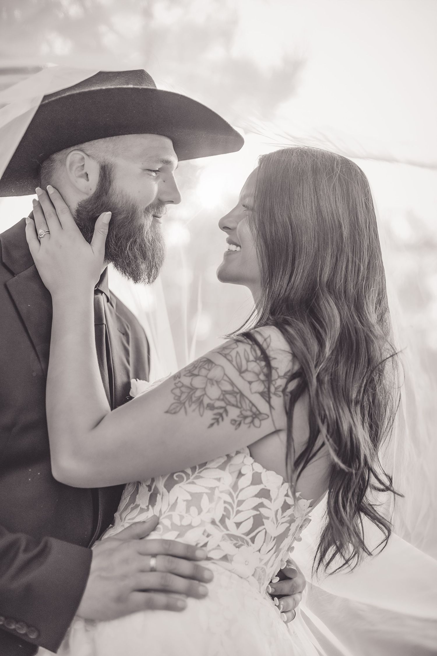 Black and white photo of smiling bride and bearded groom in cowboy hat sharing tender wedding moment.