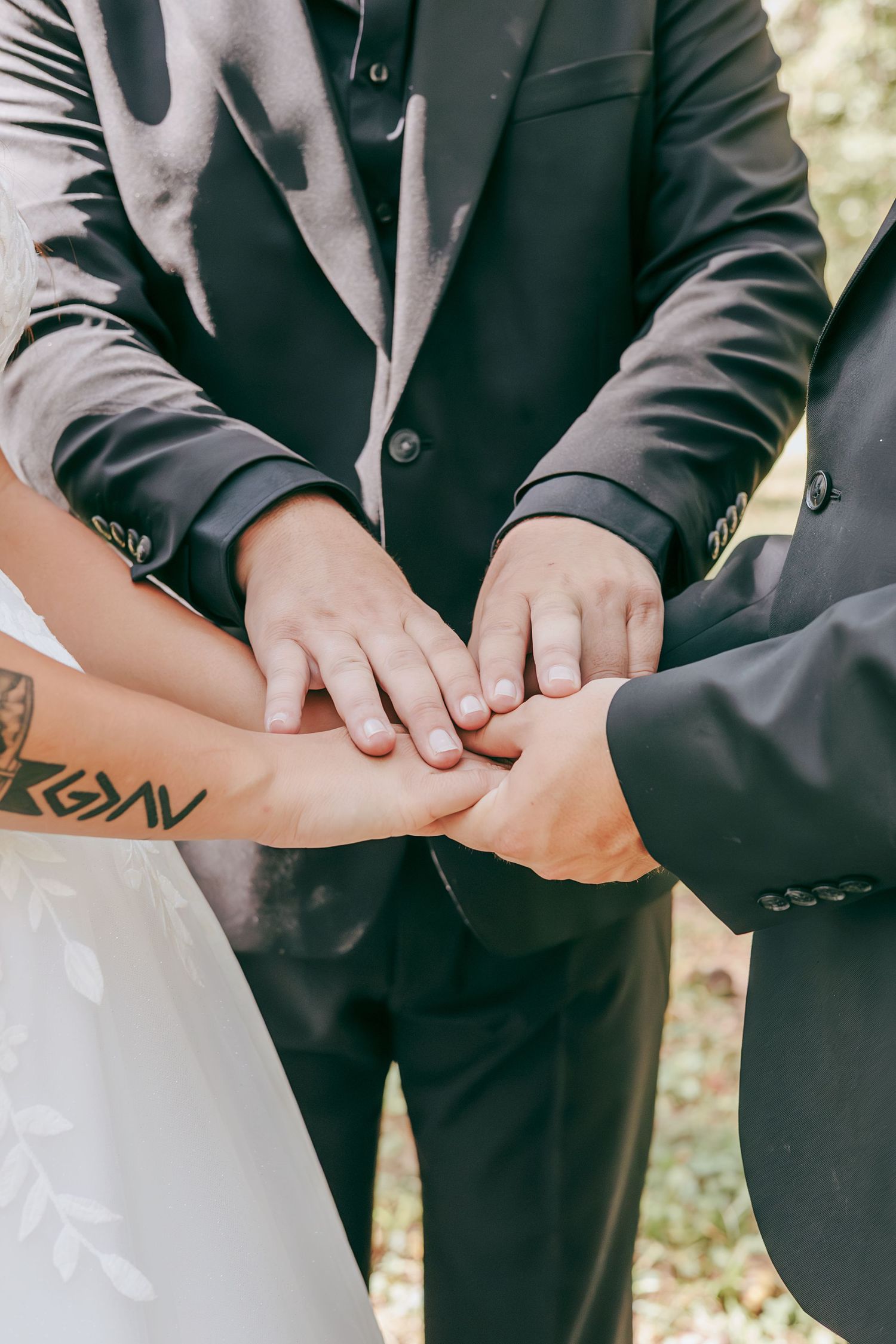 Wedding party members join hands together in a unity gesture during an outdoor woodland ceremony.