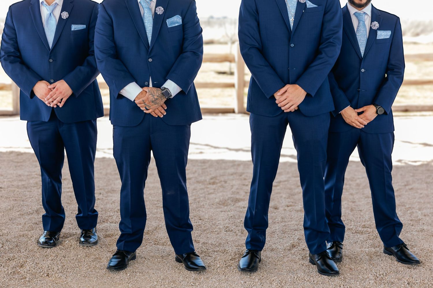 Three groomsmen in matching navy blue suits with light blue pocket squares standing together outdoors.