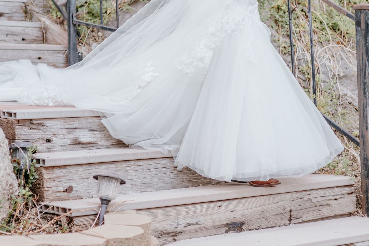 Detail shot of a bride's white ball gown train cascading down rustic wooden outdoor stairs.