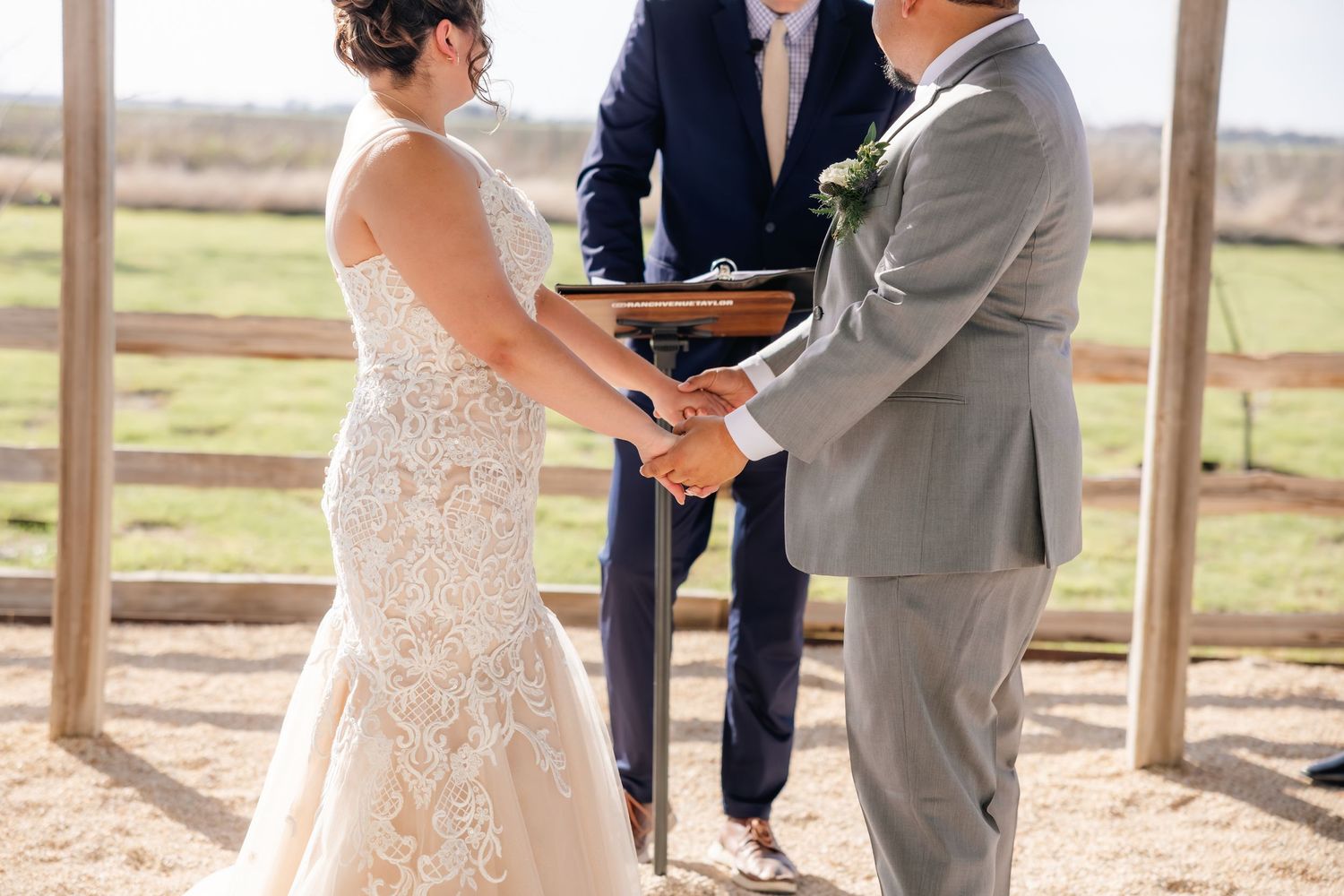 Bride and groom hold hands during outdoor wedding ceremony officiated by minister at rustic venue.