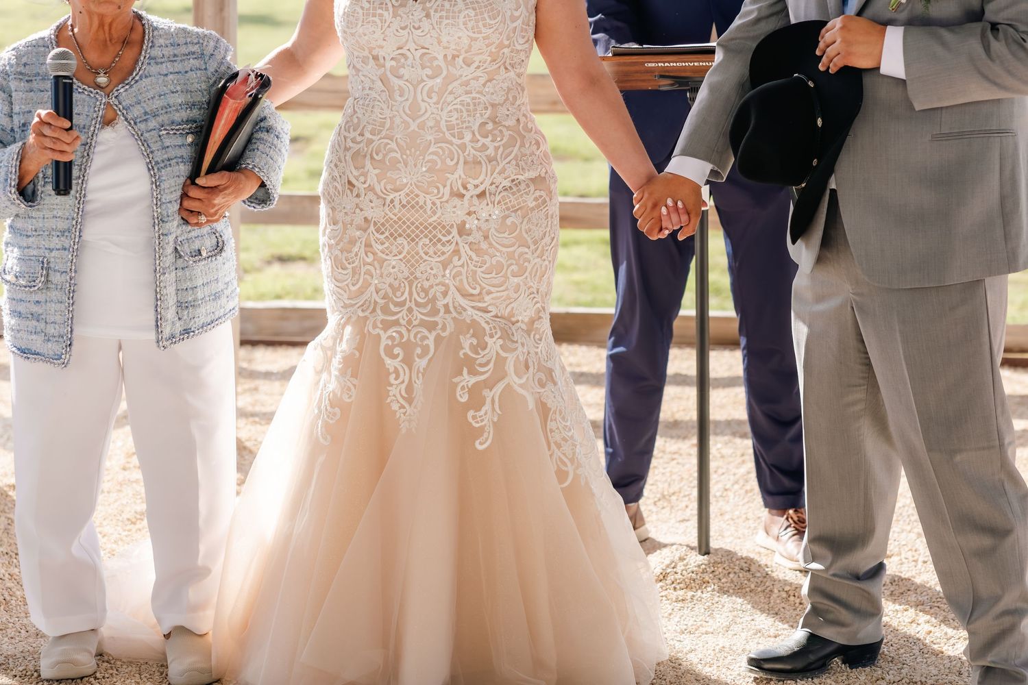 Bride in lace mermaid wedding gown holds hands with family members during an outdoor wedding ceremony.