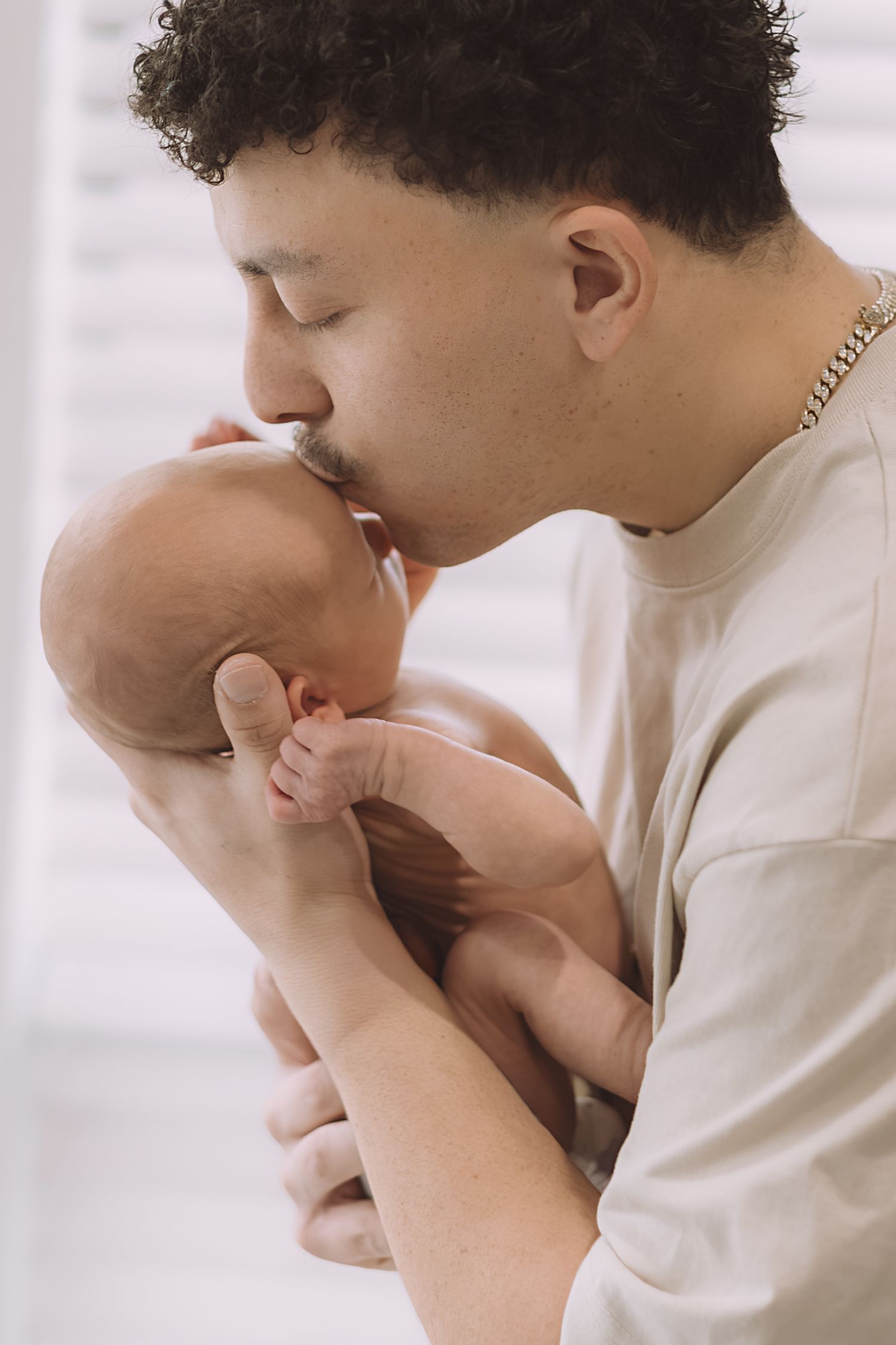 Loving father gently kissing his newborn baby on the head with closed eyes.
