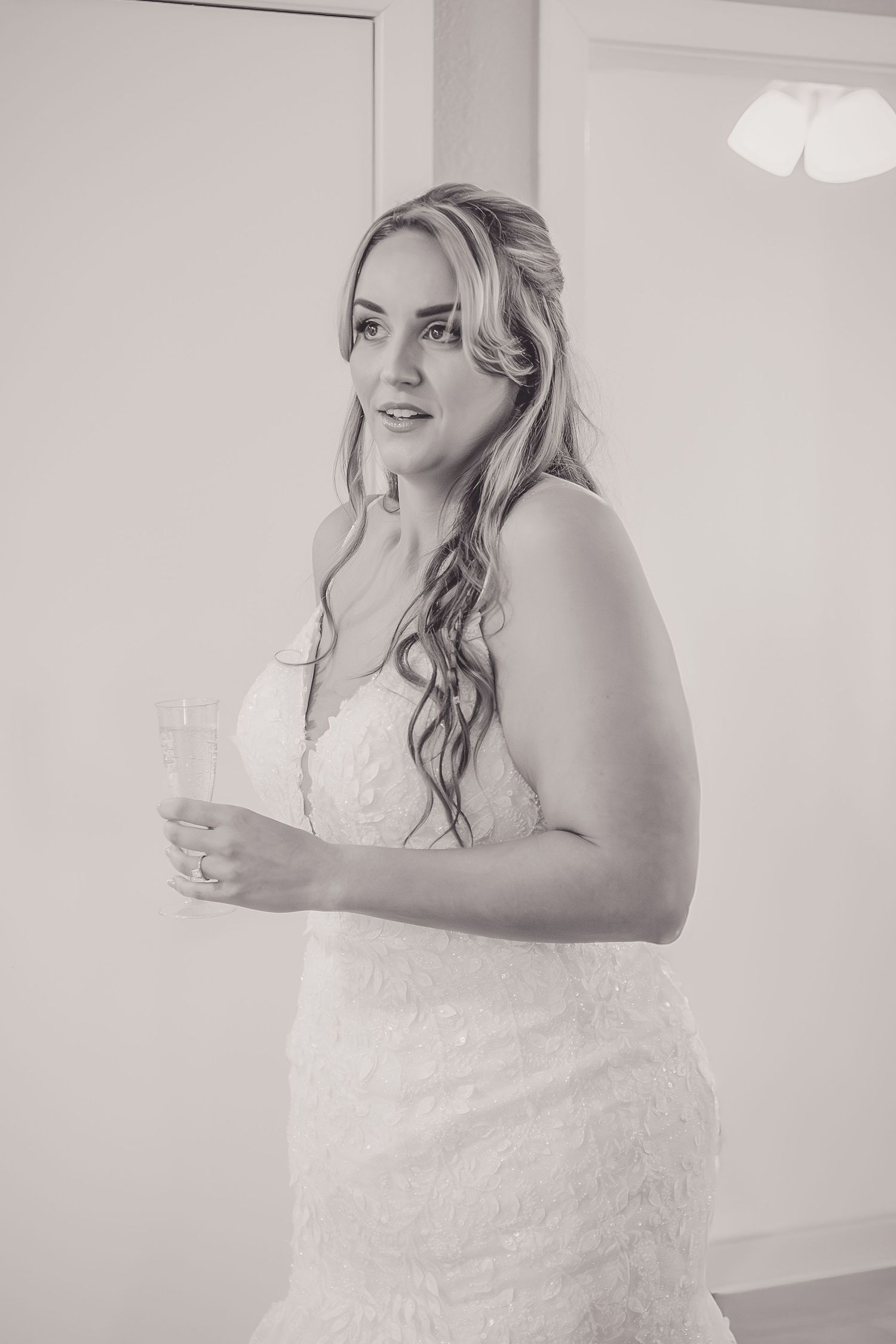Black and white portrait of a bride in a lace wedding gown holding a glass at her bridal suite.