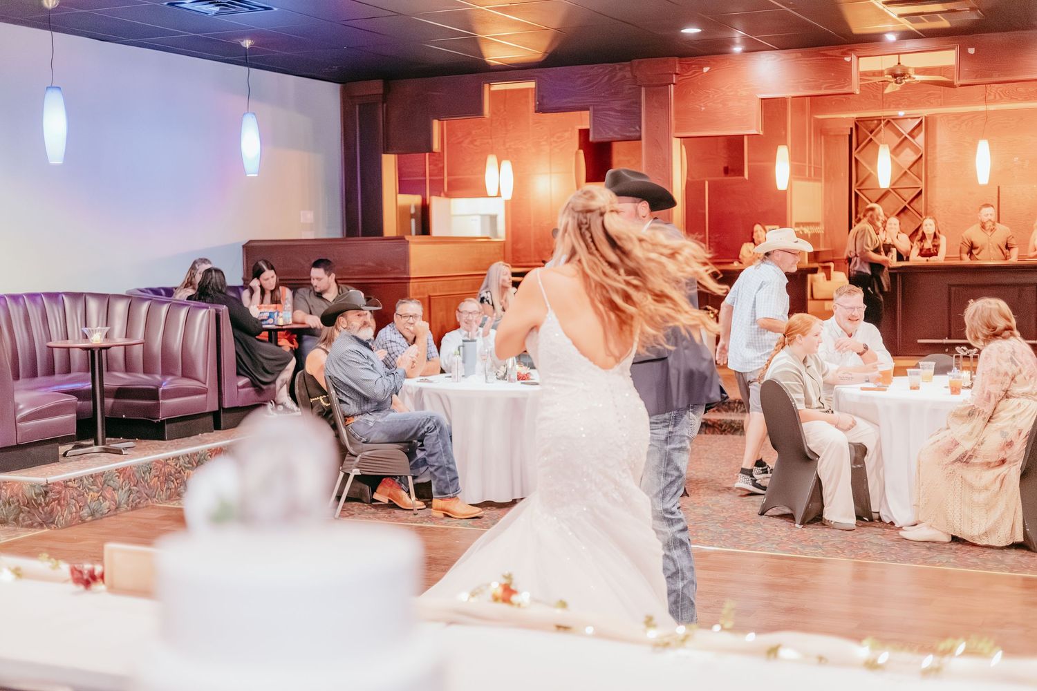 Bride and groom share first dance on the floor while wedding guests watch in a warmly lit reception venue.