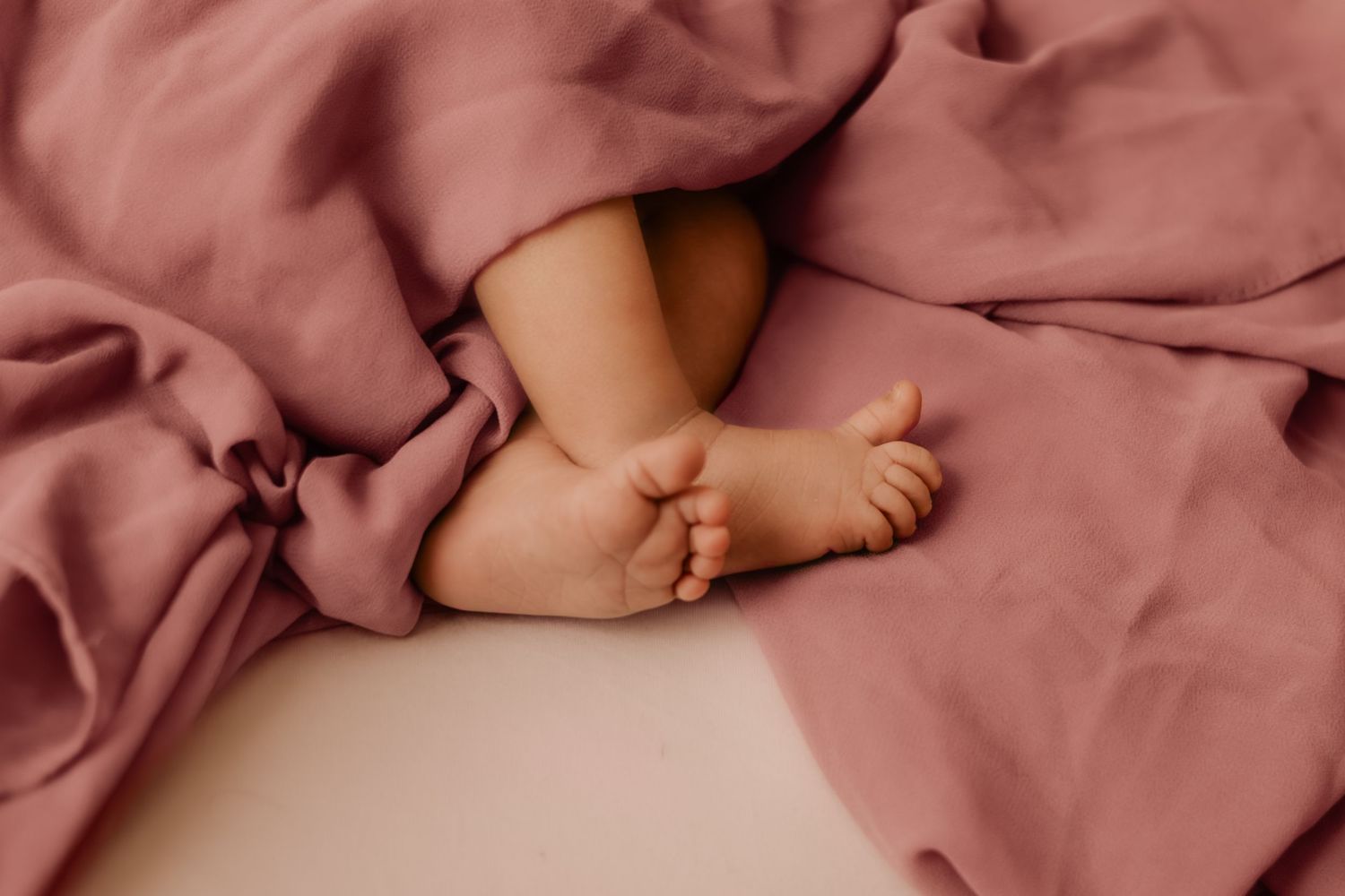Tiny newborn baby feet peek out from soft pink fabric during a newborn photography session.