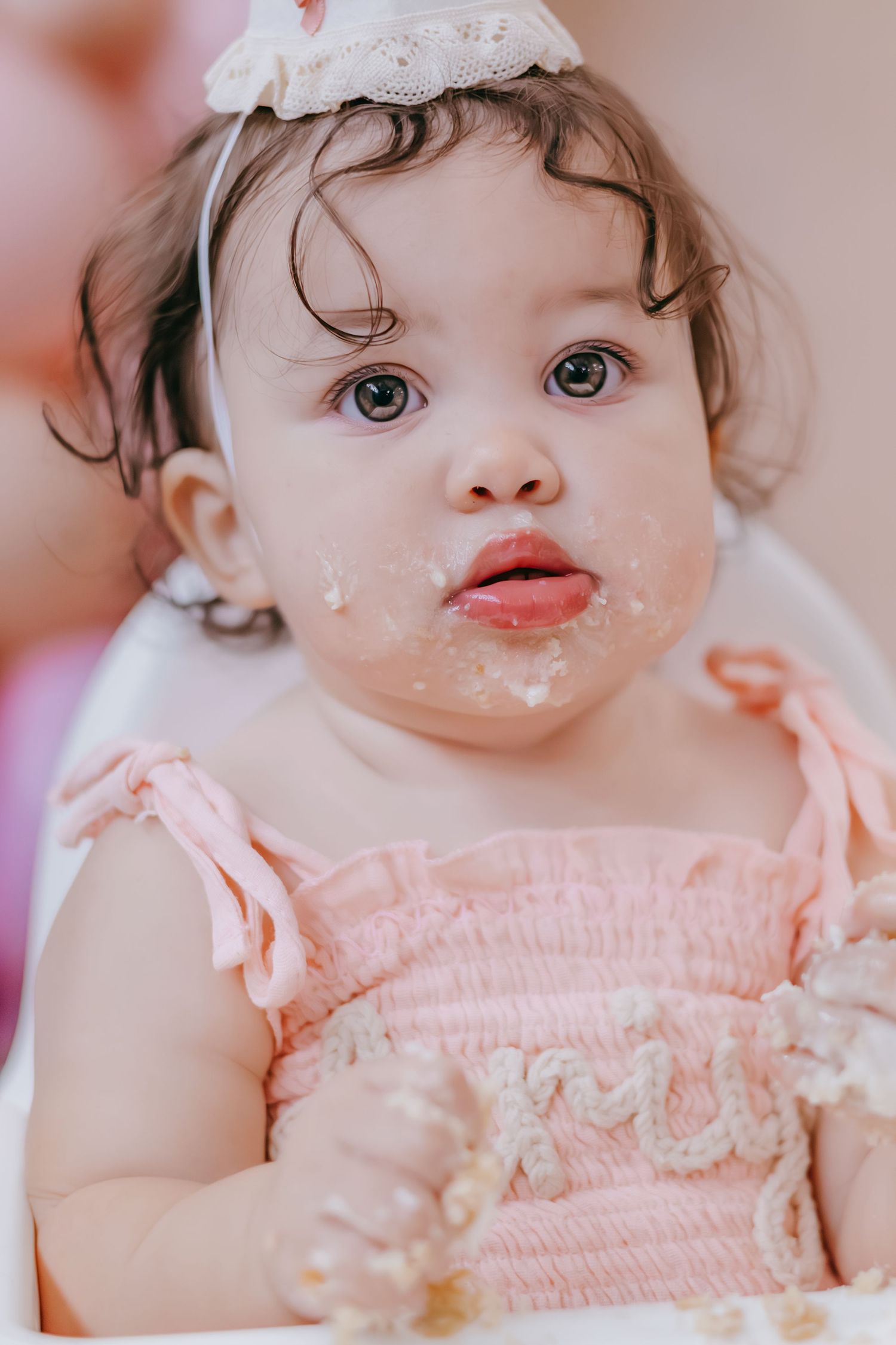 Adorable baby girl in pink dress with cake on her face celebrating her first birthday party.