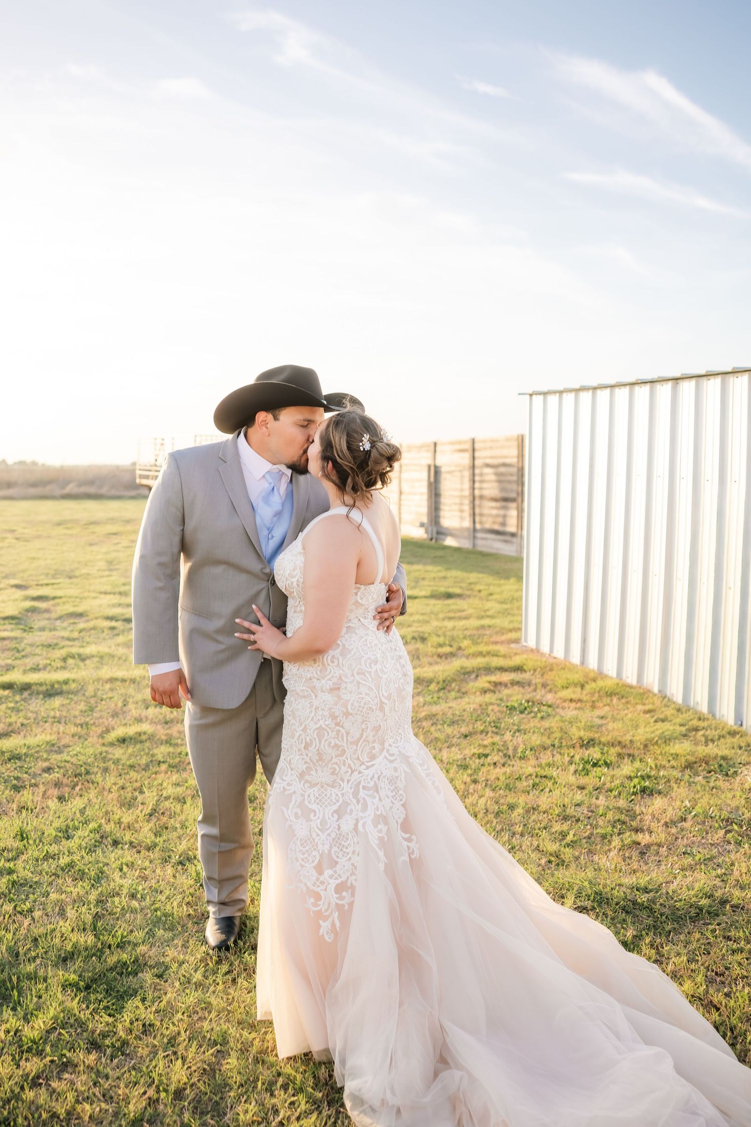A bride and groom share a tender kiss in a sunlit field at their rustic outdoor wedding.