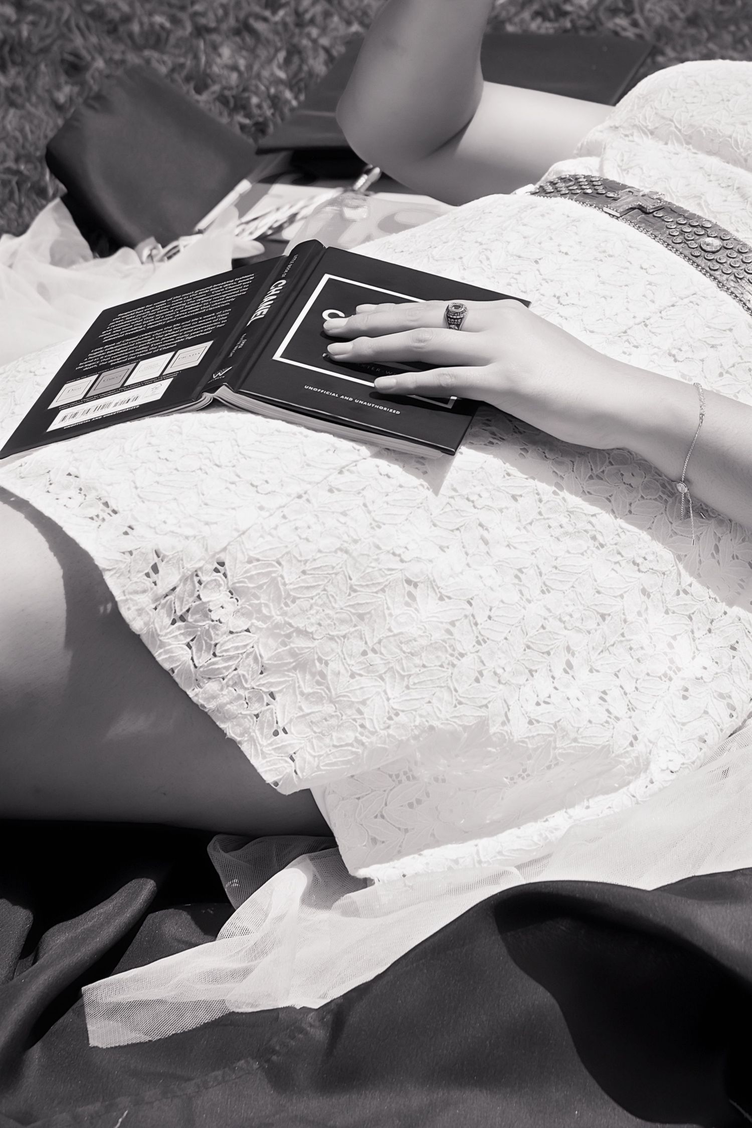 Woman in white lace dress reading a Chanel book outdoors, black and white photo.