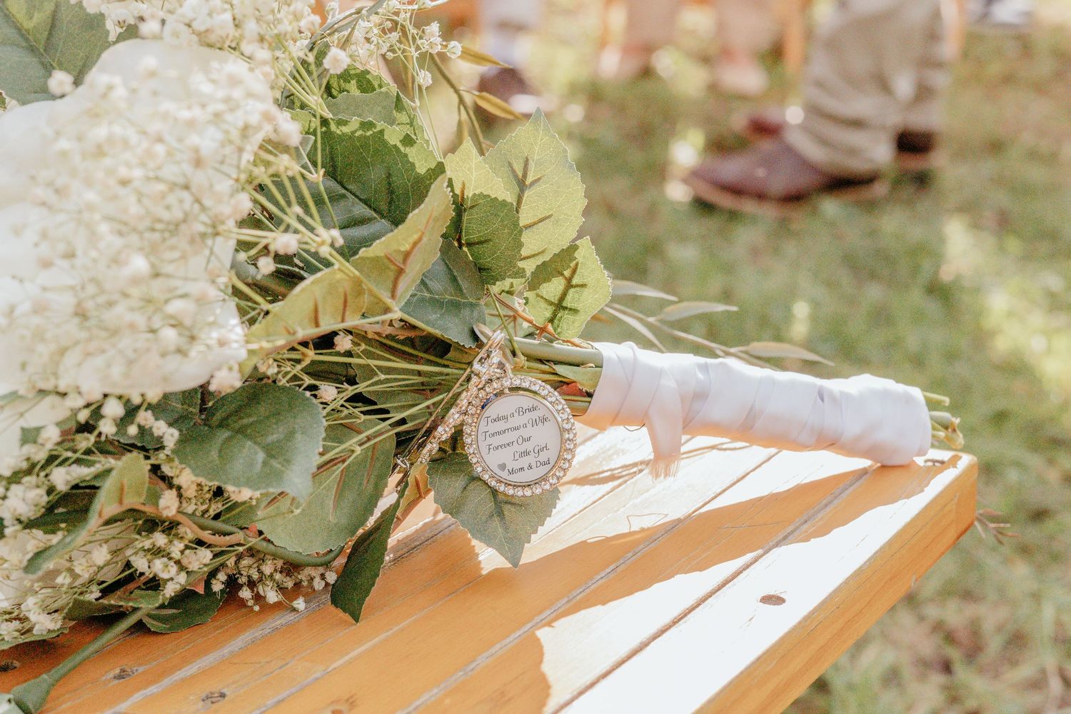 Wedding bouquet of white hydrangeas and eucalyptus with a charm tag resting on a wooden bench.