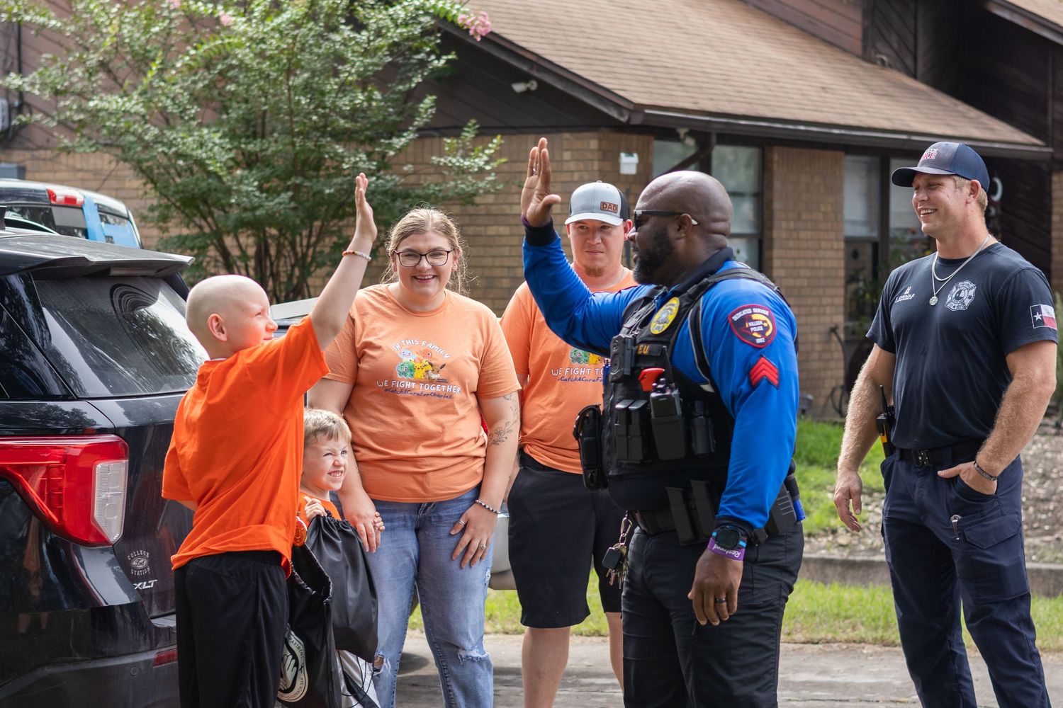A police officer and firefighter high-fiving community members outdoors during a friendly neighborhood engagement event.