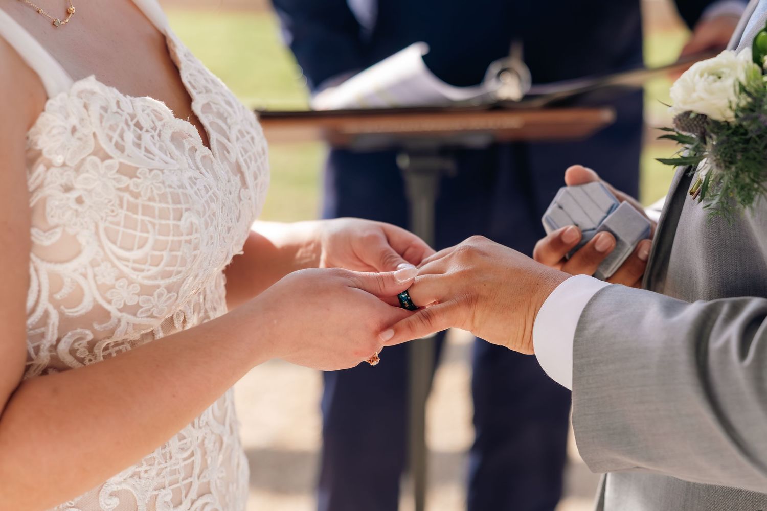 Bride and groom exchanging wedding rings during outdoor ceremony, close-up of hands with lace wedding dress.