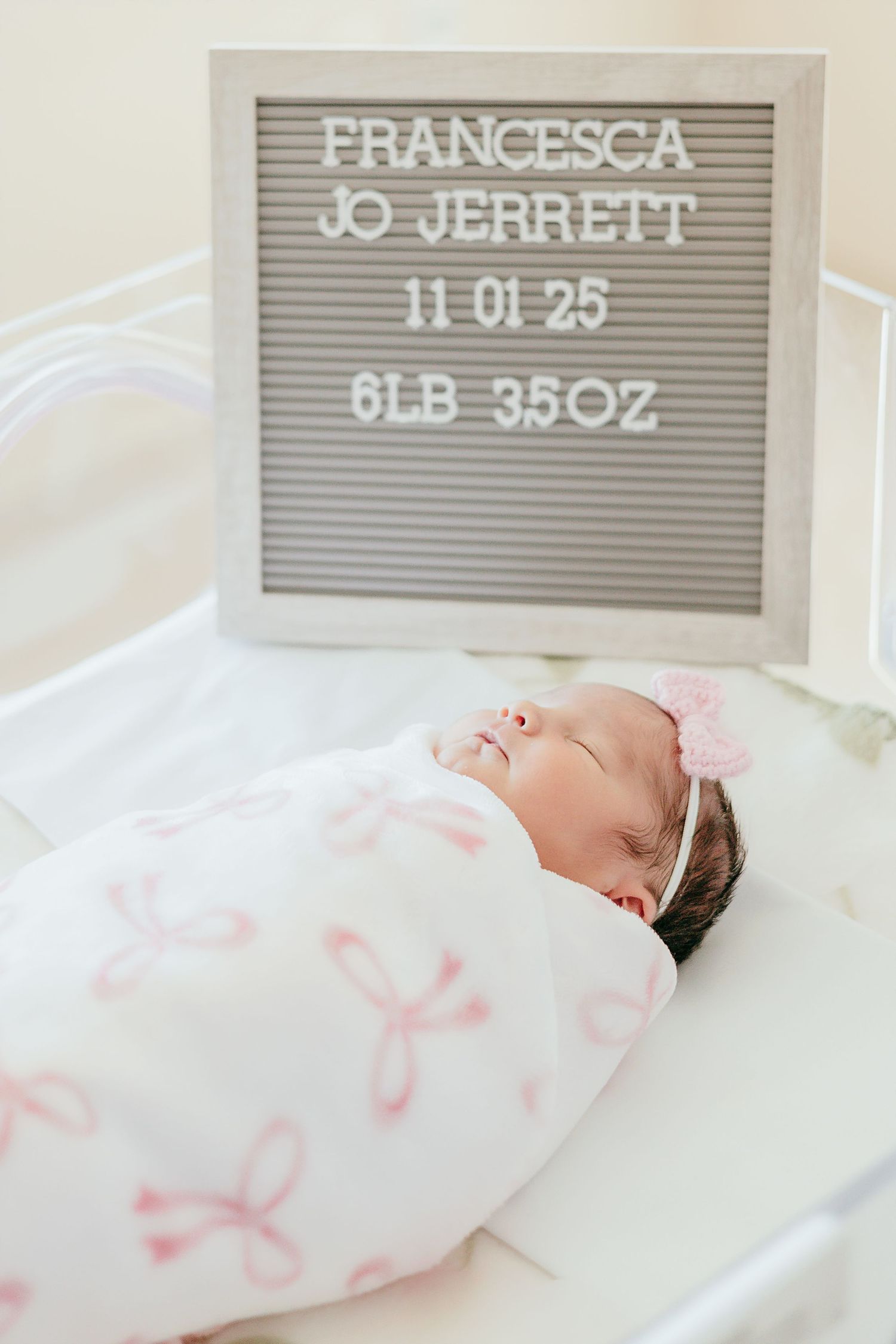 Newborn baby girl Francesca Jo Jerrett swaddled in pink bow blanket beside birth announcement letter board.
