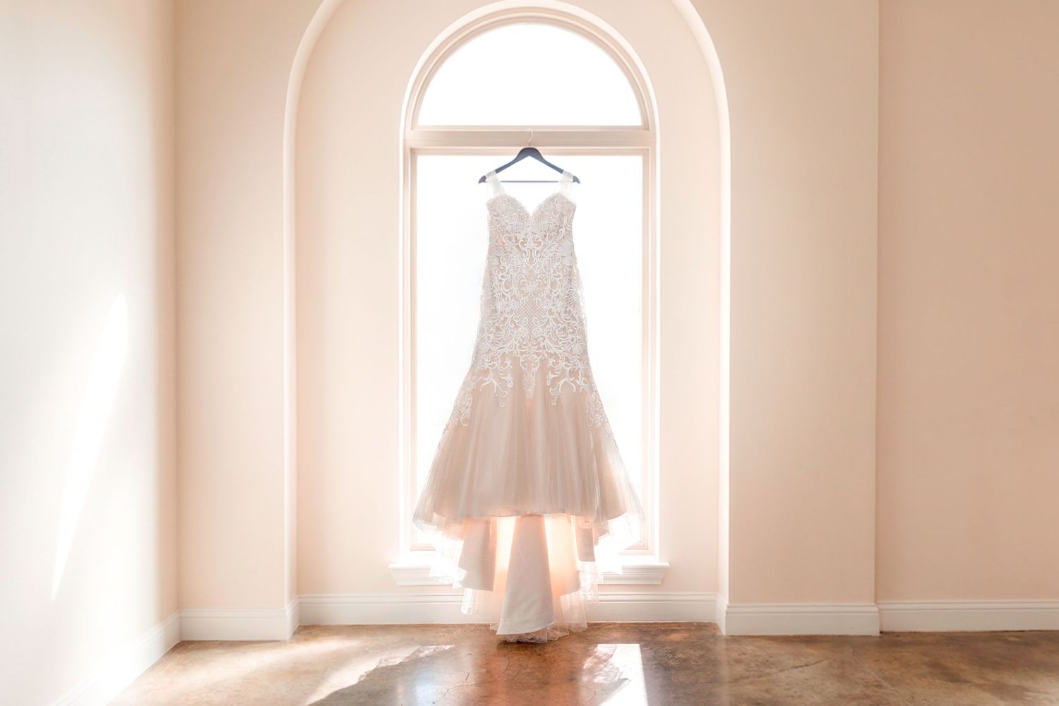 Elegant lace mermaid wedding dress hanging in an arched window with soft natural light.