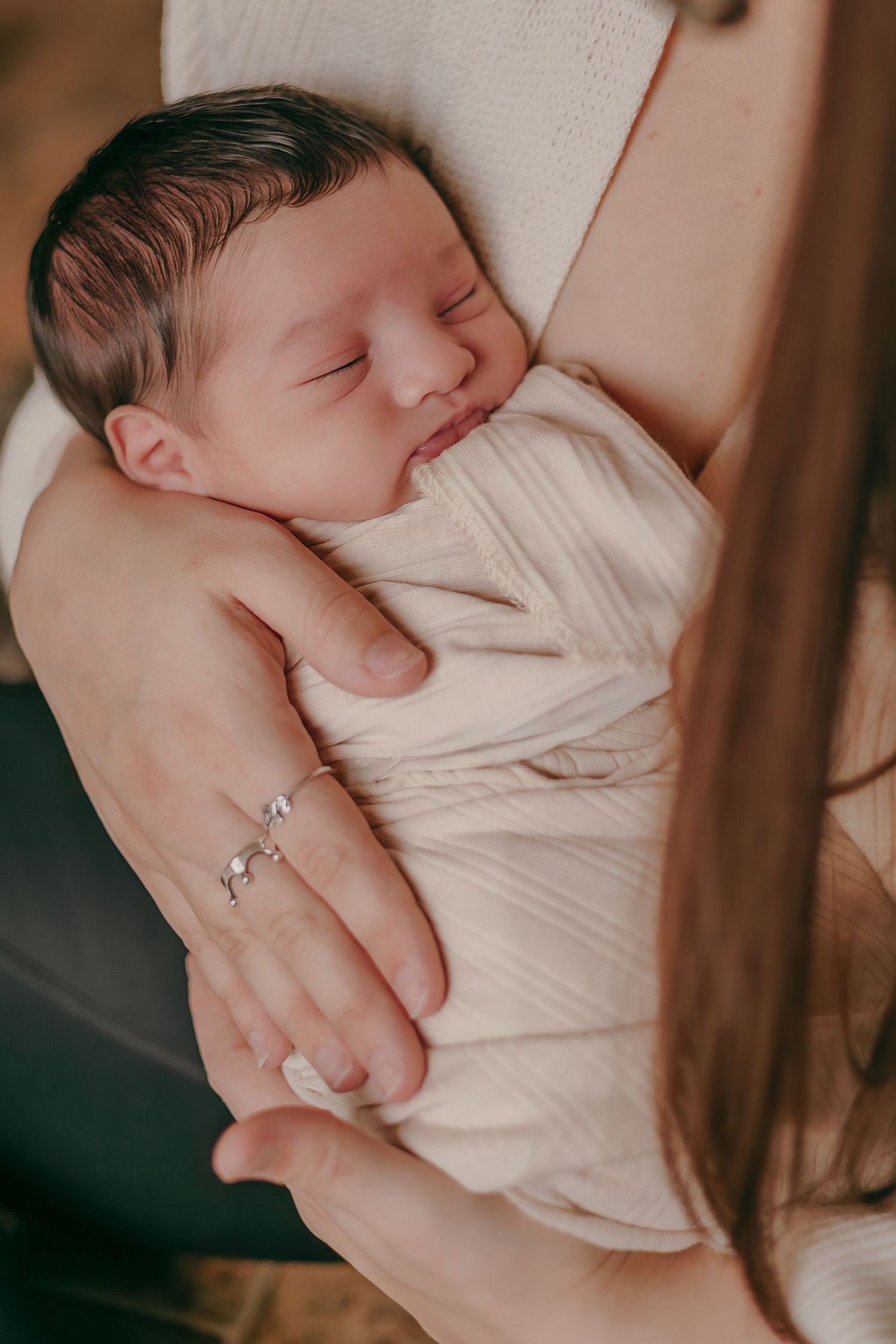 Sleeping swaddled newborn baby cradled in mothers arms with delicate bracelet visible.