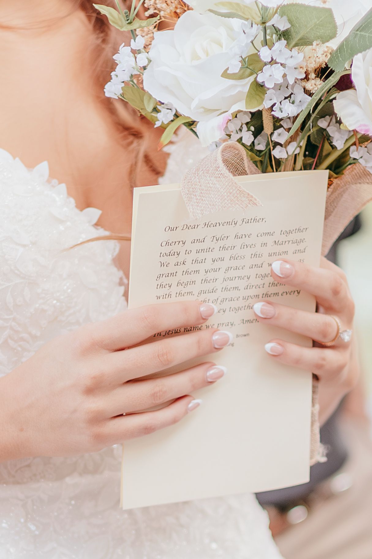 Bride holding bouquet and handwritten wedding prayer card in lace gown.