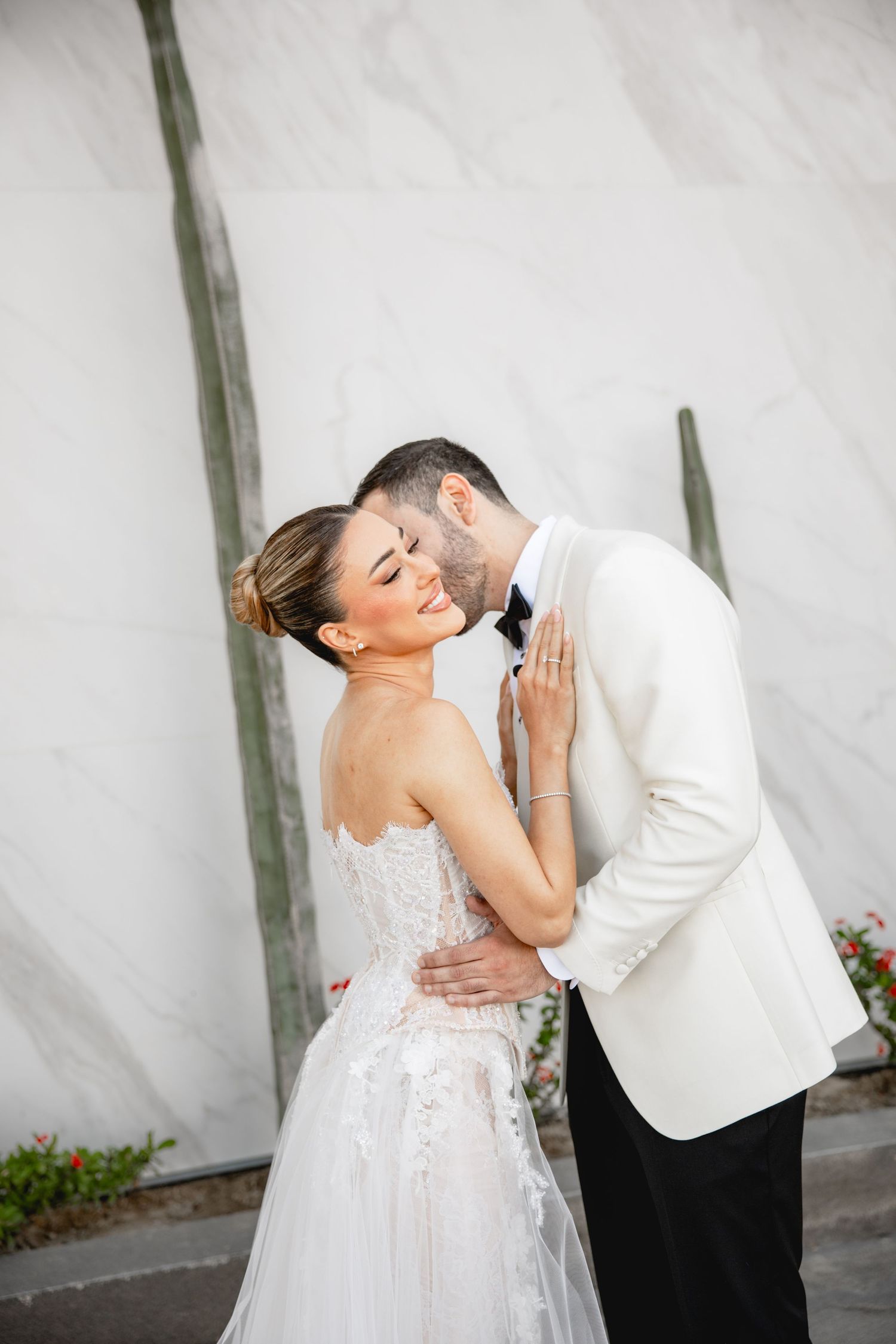 Romantic wedding couple sharing a tender moment against a white wall with green accents.