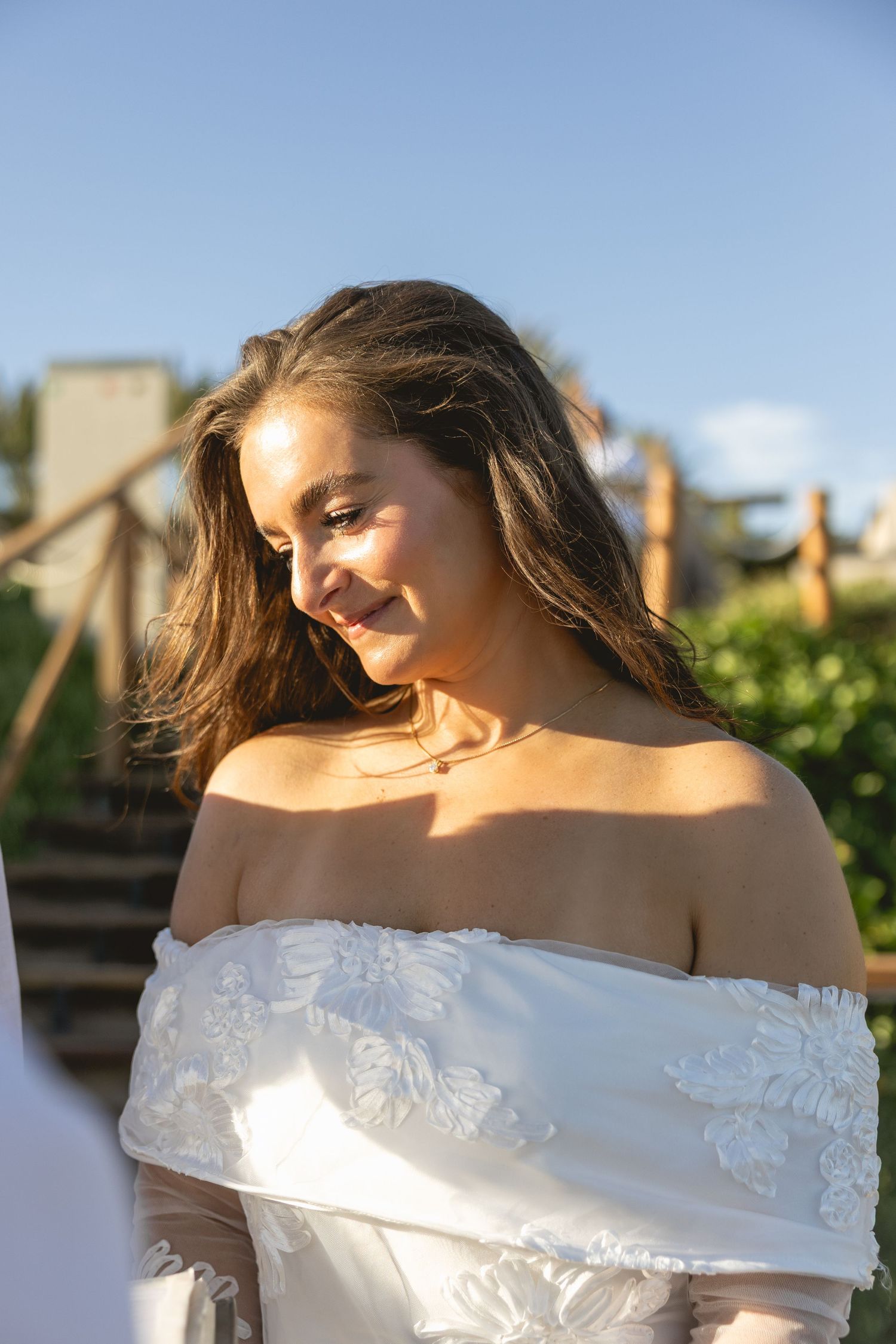 Woman in off-shoulder white dress posing in golden sunlight.