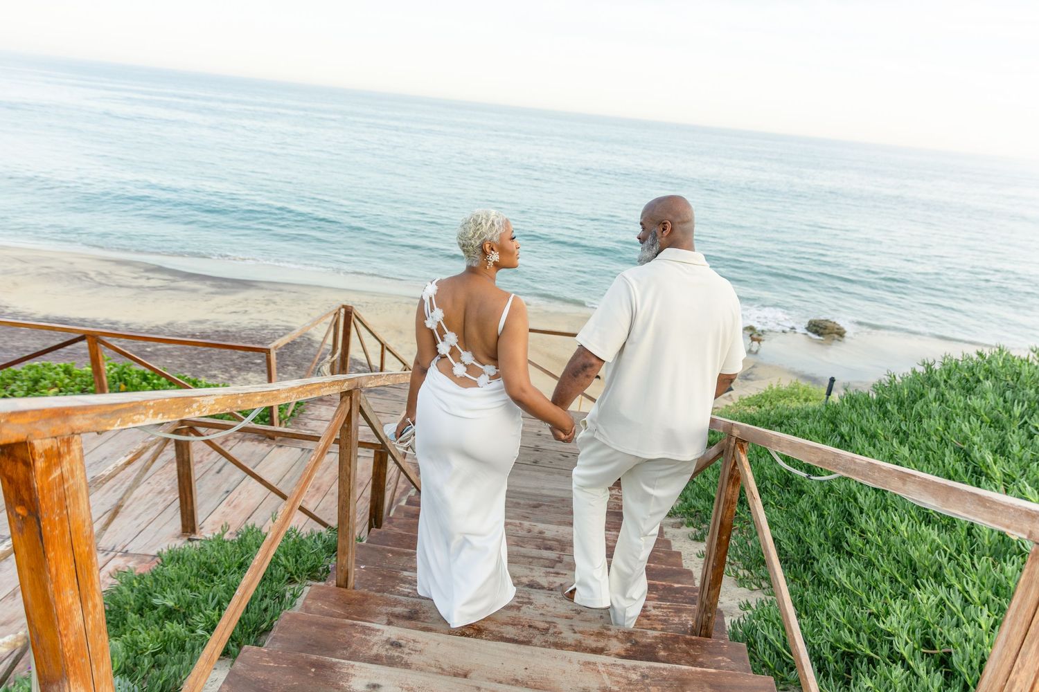 Couple in white clothing walking along coastal pathway with ocean view.