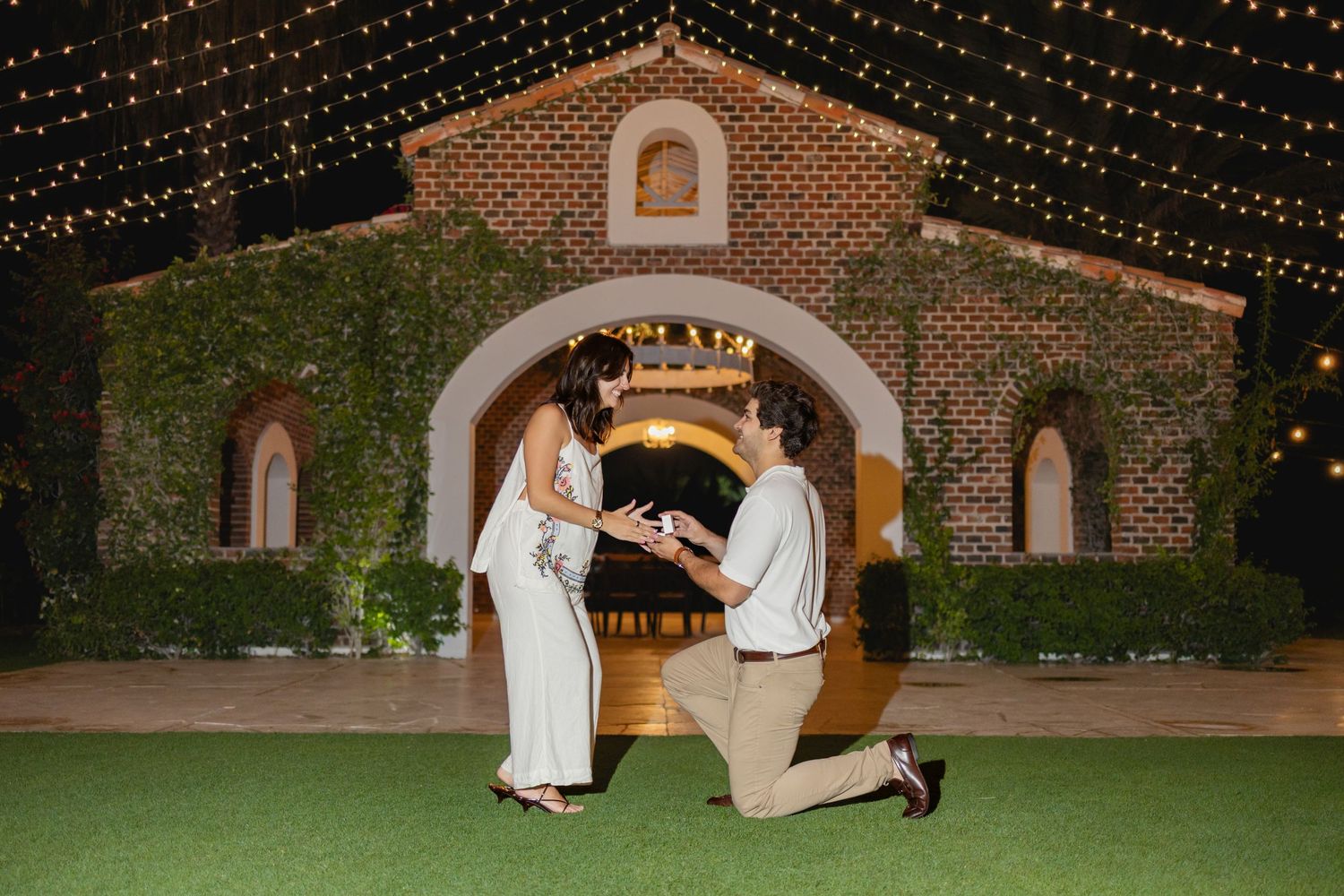 Romantic outdoor wedding ceremony at night with string lights illuminating a brick courtyard.